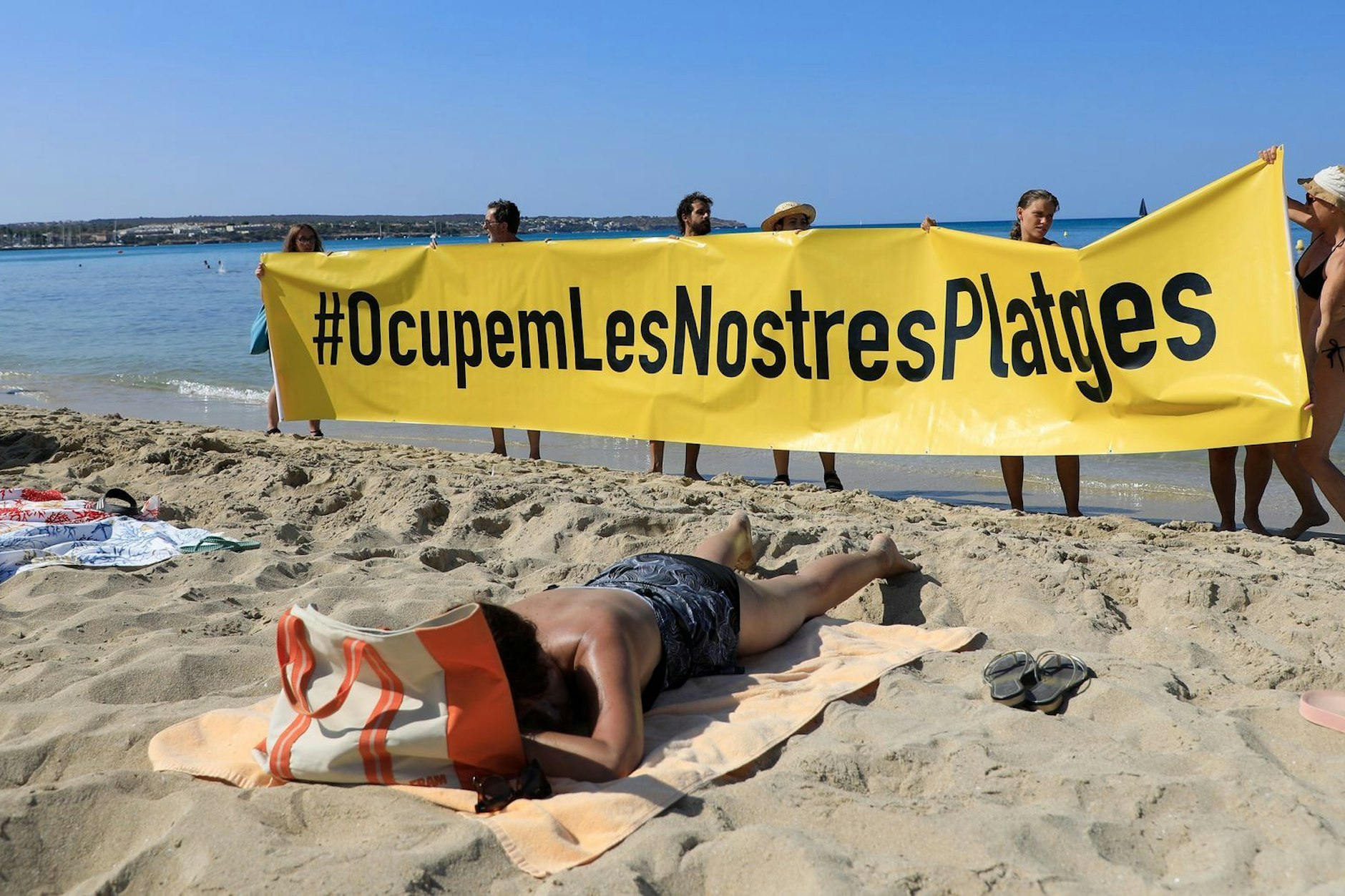 Leute halten an einem Strand auf Mallorca ein Banner mit der Schrift „#Besetzen wir unsere Strände“ aus Protest gegen den Massentourismus auf der Balearen-Insel. 