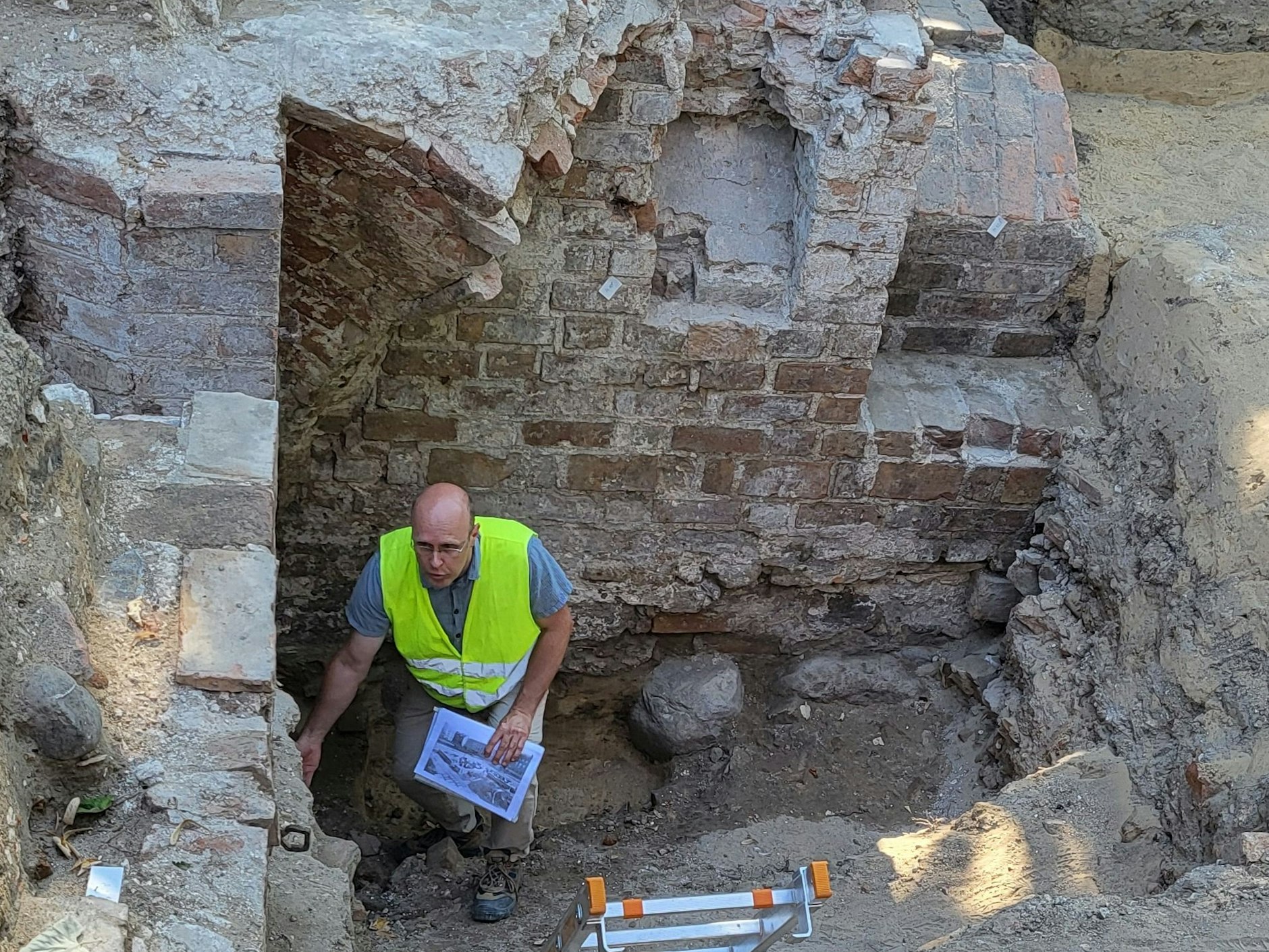 Grabungsleiter Gerson Jeute auf dem Boden der Grube im Haus Hoher Steinweg 15. Gut sichtbar die Findlinge der untersten Fundamentschicht, darüber Ziegel im Klosterformat. Über seinem Kopf der Bogenansatz für ein Kreuzrippengewölbe. Links ein Eingang.
