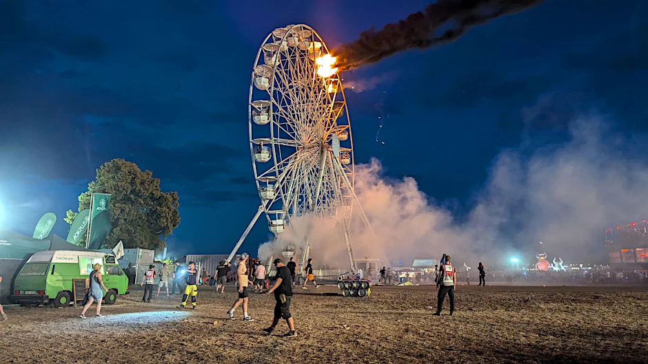 Besucher des Highfield-Festivals und Helfer blicken auf das brennende Riesenrad.