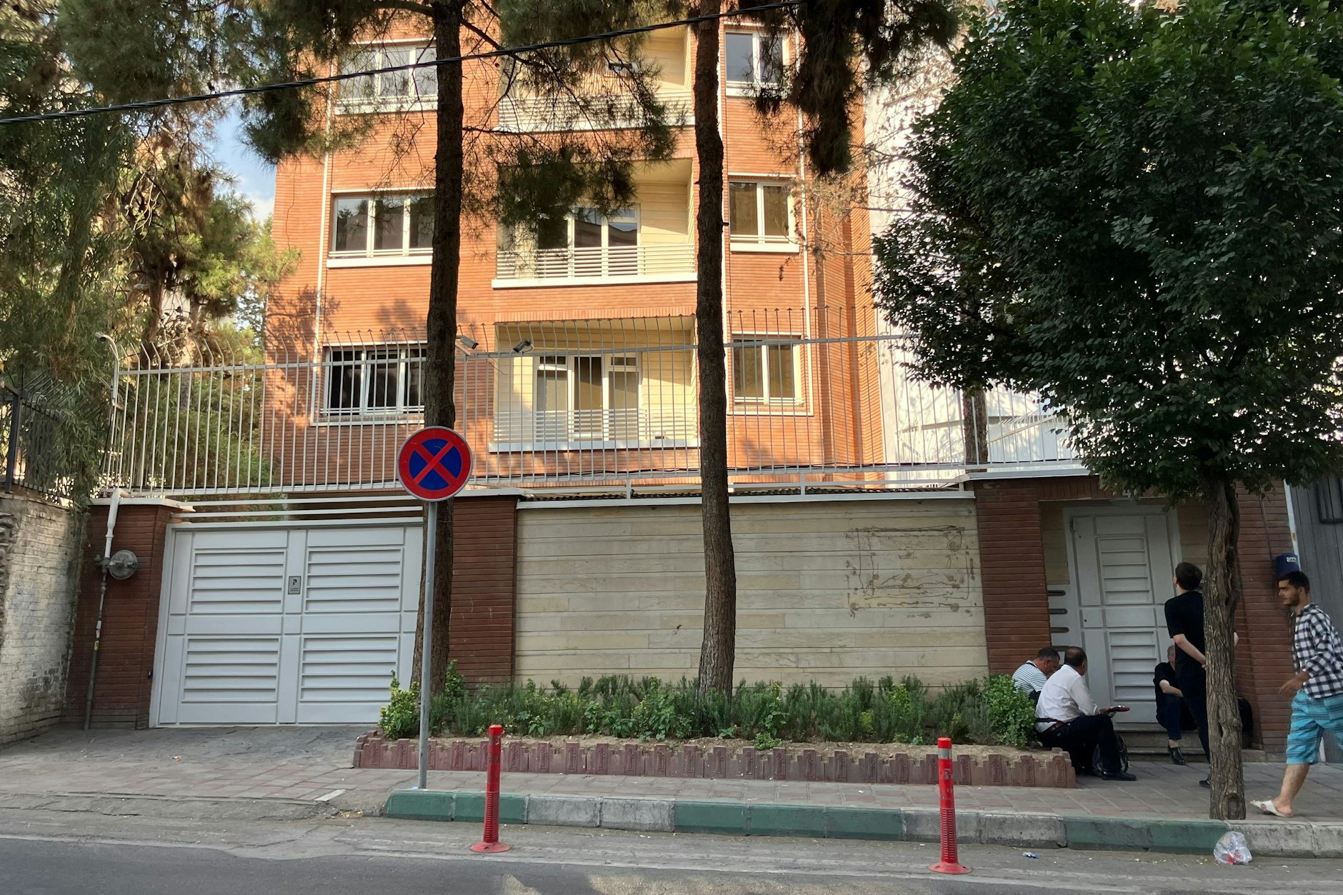 Ein paar Menschen stehen und sitzen vor dem versiegelten Eingangsbereich des Deutschen Sprachinstituts in Teheran (DSIT). Irans Behörden haben das Institut schließen lassen. Sicherheitskräfte versiegelten das Gebäude im Norden der Millionenmetropole, wie Augenzeugen berichteten. Das Webportal Nurnews, das dem iranischen Sicherheitsrat nahesteht, deutete den Schritt als Reaktion auf die Schließung des Islamischen Zentrum Hamburg (IZH). Foto: dpa +++ dpa-Bildfunk +++