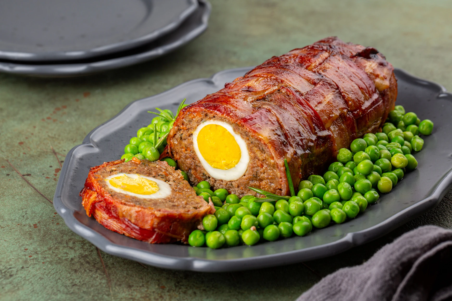 Rezept für Omas Falschen Hasen – eine saftige Hackfleischrolle, die in appetitlichen Scheiben geschnitten wird. Die goldbraune Kruste ist perfekt gebacken, und in der Mitte der Scheiben sieht man das hartgekochte Ei.