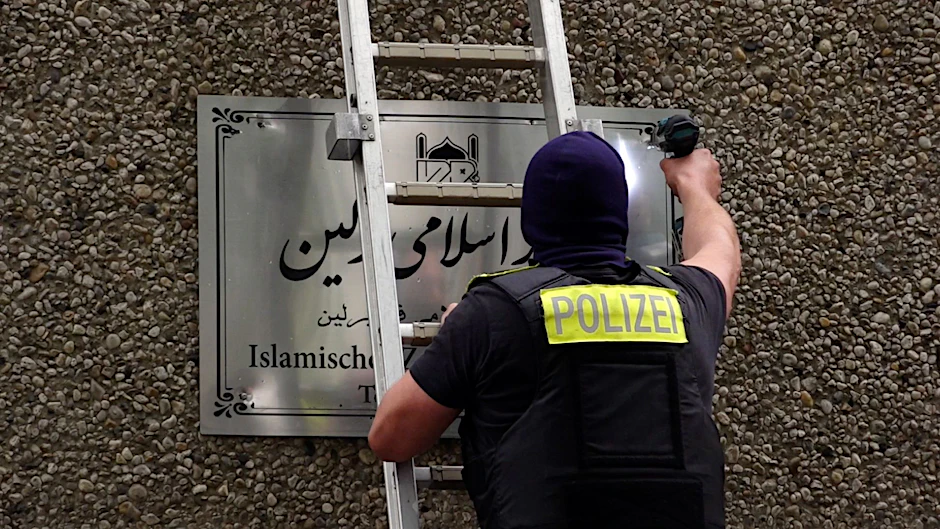 Ein Polizist entfernt ein Hinweisschild vom Islamischen Zentrum Berlin in der Ordensmeisterstraße. Im Zusammenhang mit dem Verbot des Islamischen Zentrums Hamburg und seiner Teilorganisationen hat die Polizei in Berlin vier Objekte durchsucht.