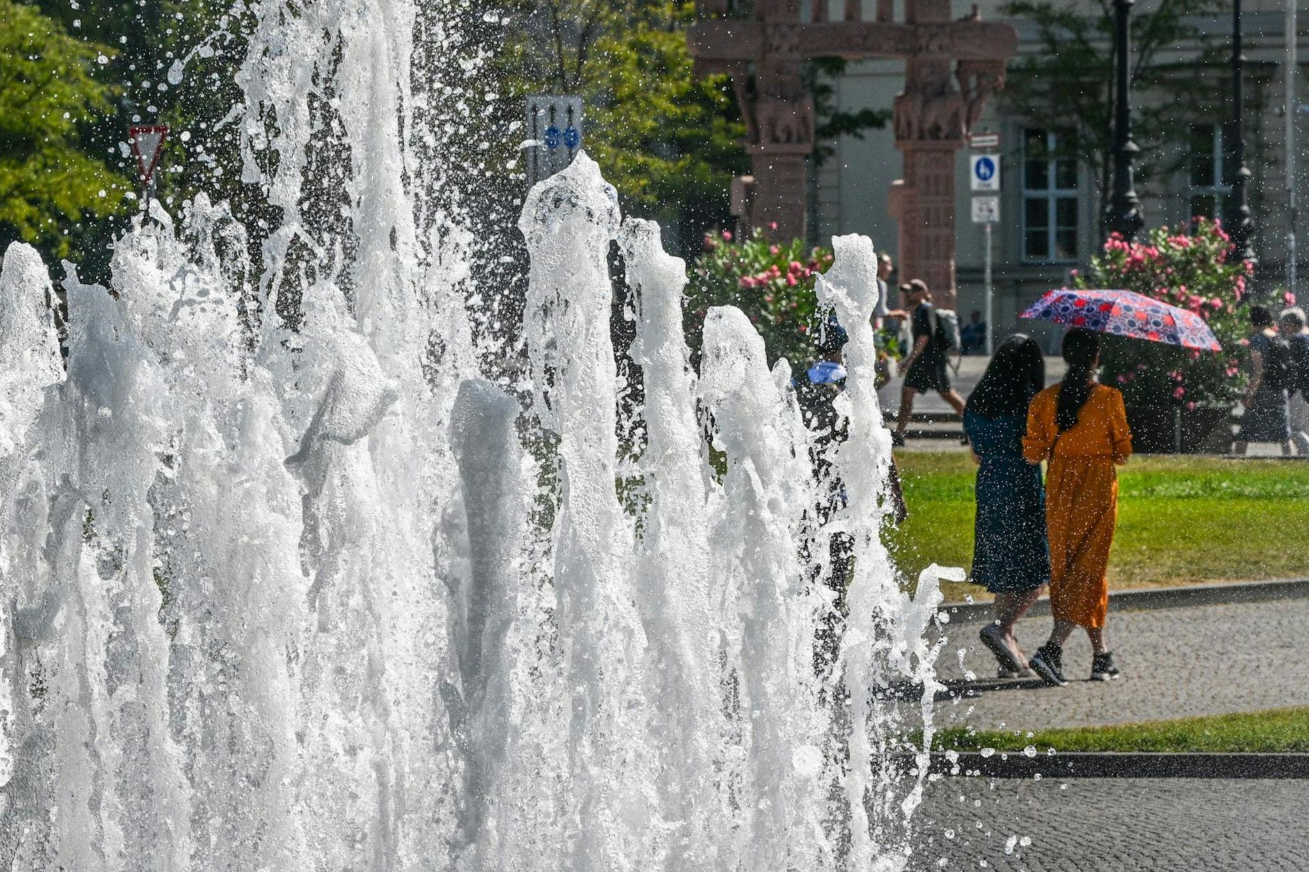 Mit einem Regenschirm schützen sich Passantinnen hinter den Fontänen des Brunnens im Lustgarten gegen die Sonne. 