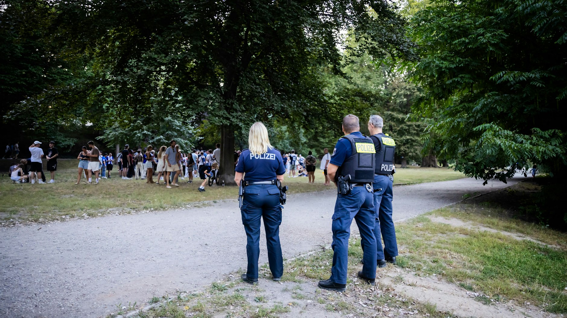 Drei Polizisten verfolgen mit Abstand das Treffen von Fabian Reese mit Fans von Hertha BSC im Lietzenseepark.