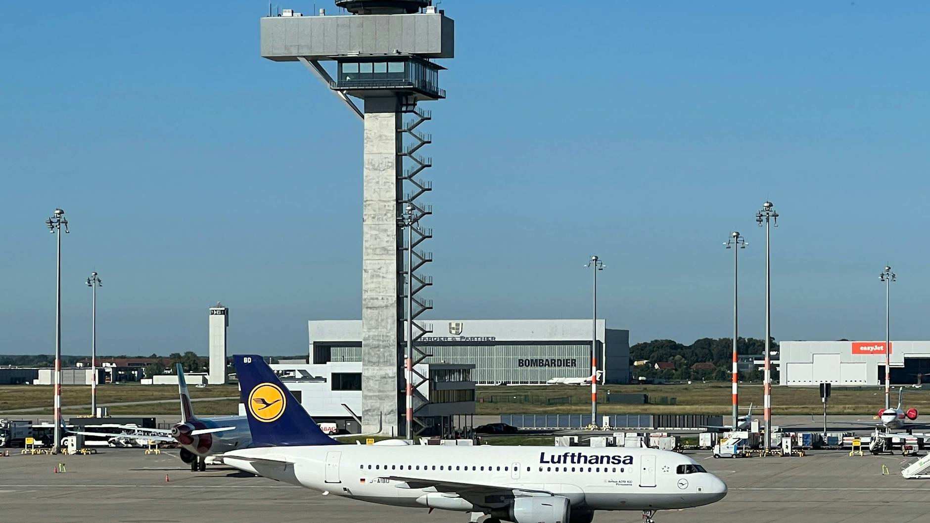 Am BER-Tower rollt eine Lufthansa-Maschine vorbei. Oben auf dem Kontrollturm sitzen die Lotsen der Flugsicherung.