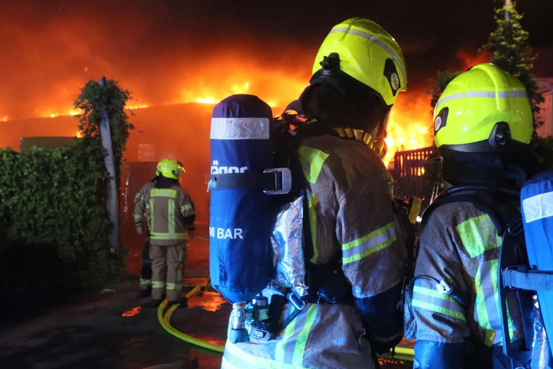Feuerwehrleute schützen erfolgreich zwei benachbarte Einfamilienhäuser vor dem Übergreifen der Flammen. Dichte Rauchwolken füllen den Himmel.