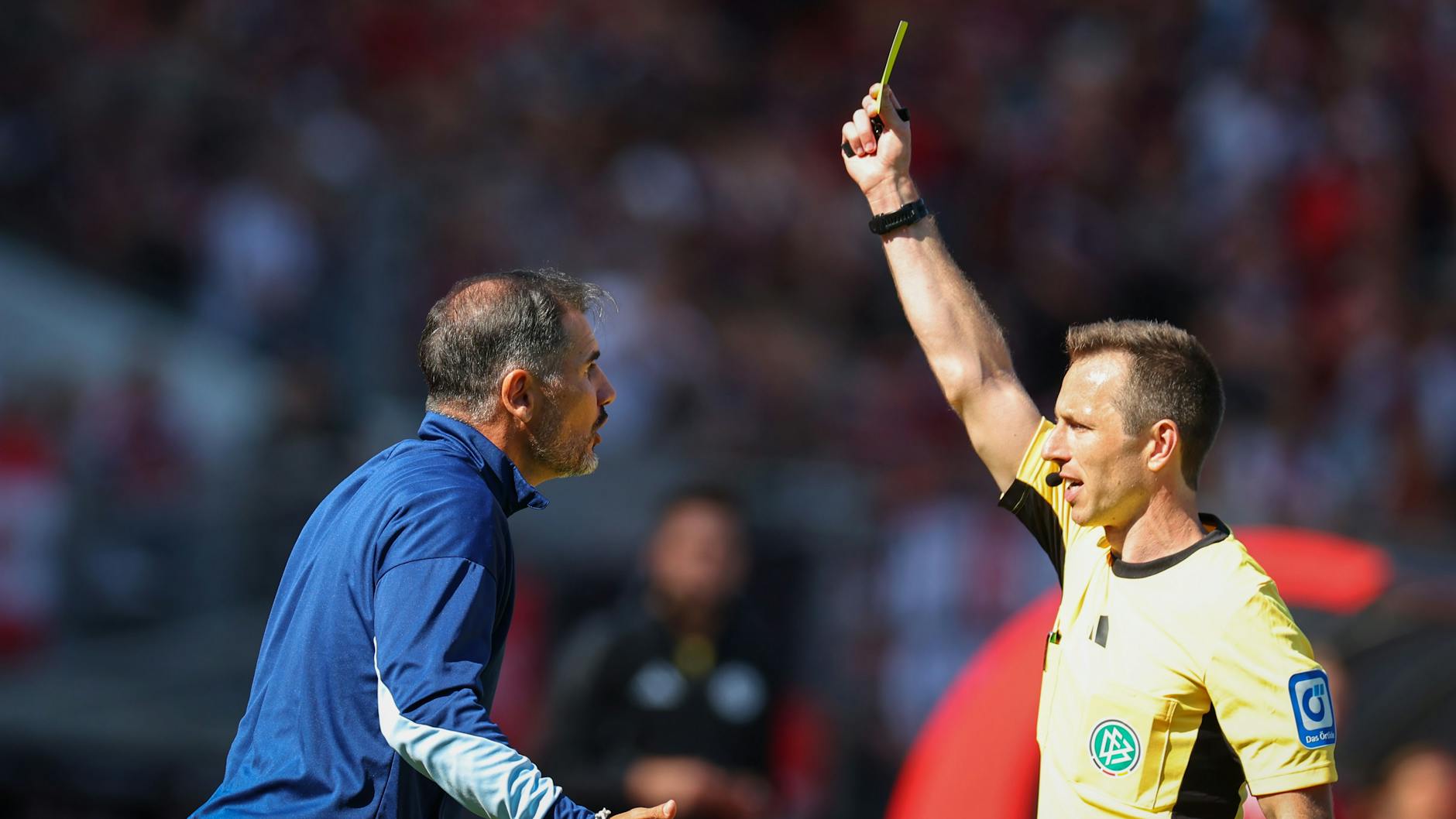 2Schiedsrichter Lukas Benen (r.) zeigt Herthas Trainer Cristian Fiel die gelbe Karte.