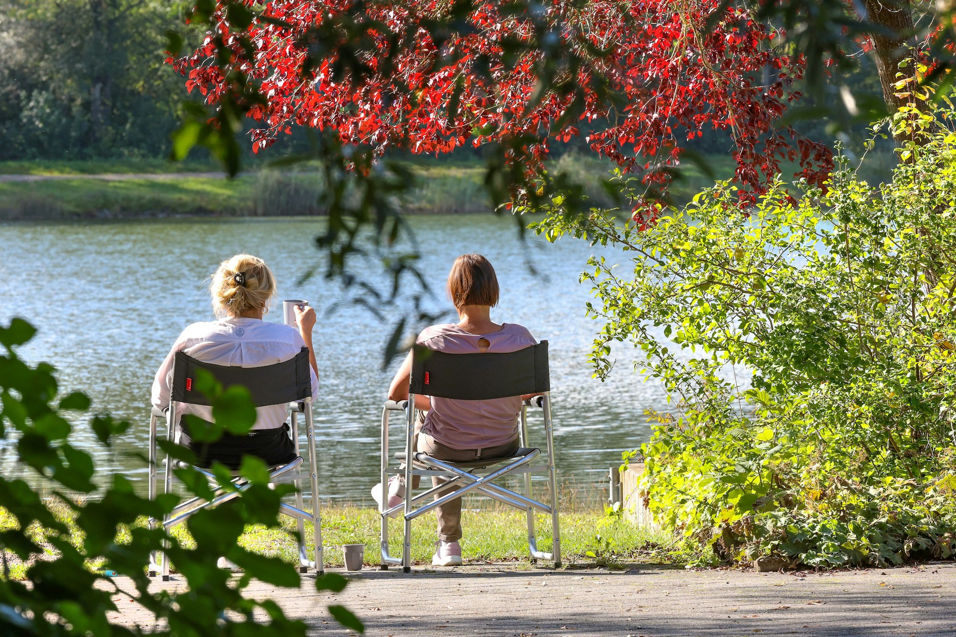 Zwei Frauen sitzen auf Campingstühlen in der Sonne und schauen aufs Wasser. 