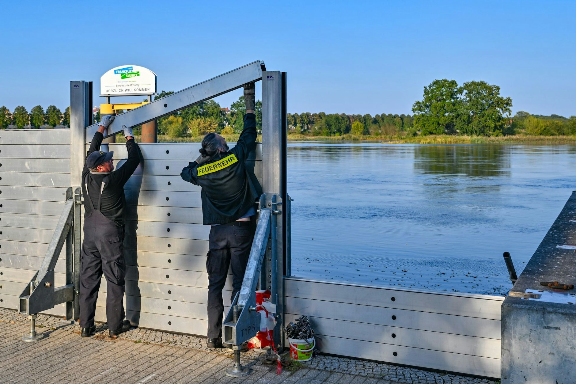 Zwei Kameraden der Freiwilligen Feuerwehr errichten eine mobile Hochwasserschutzwand am deutsch-polnischen Grenzflusses Oder. Noch ist unsicher, wie ernst die Hochwasserlage in Brandenburg wirklich wird.