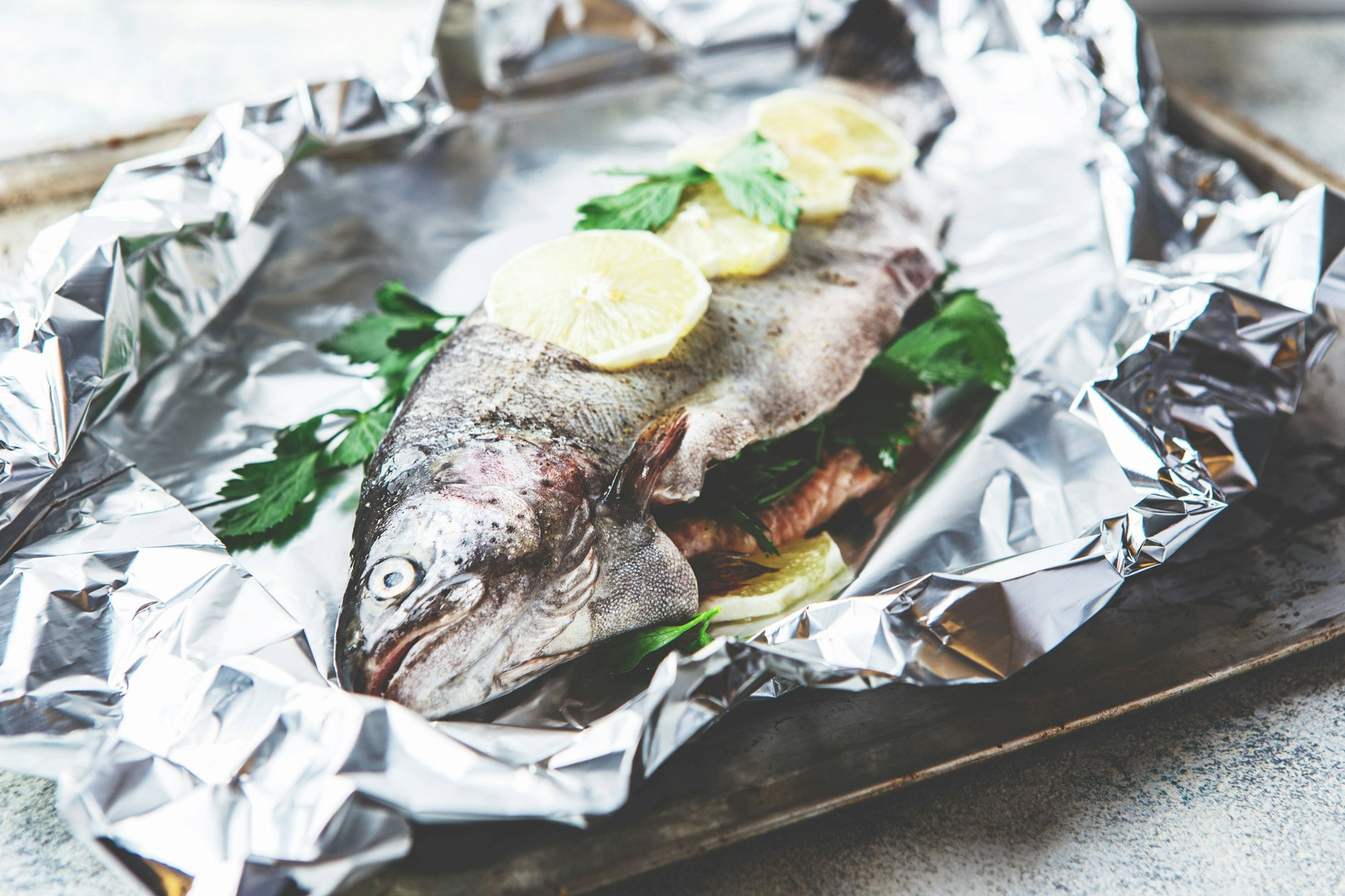 Rezept: Der Lachs wird in Alufolie eingewickelt, damit er schonend im eigenen Saft garen kann. Die Zitrone und frischen Kräuter verleihen ihm ein frisches Aroma, während die Alufolie dafür sorgt, dass der Fisch besonders saftig und zart bleibt.