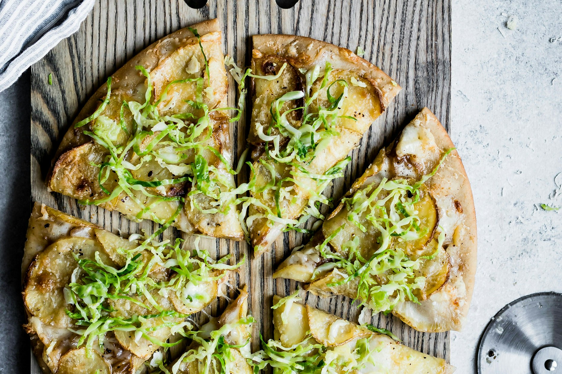 Kartoffelpizza mit Rosenkohl auf einem rustikalen Holzbrett serviert macht nicht nur optisch etwas her. Es schmeckt auch super lecker und ist mit diesem Rezept einfach zuzubereiten.