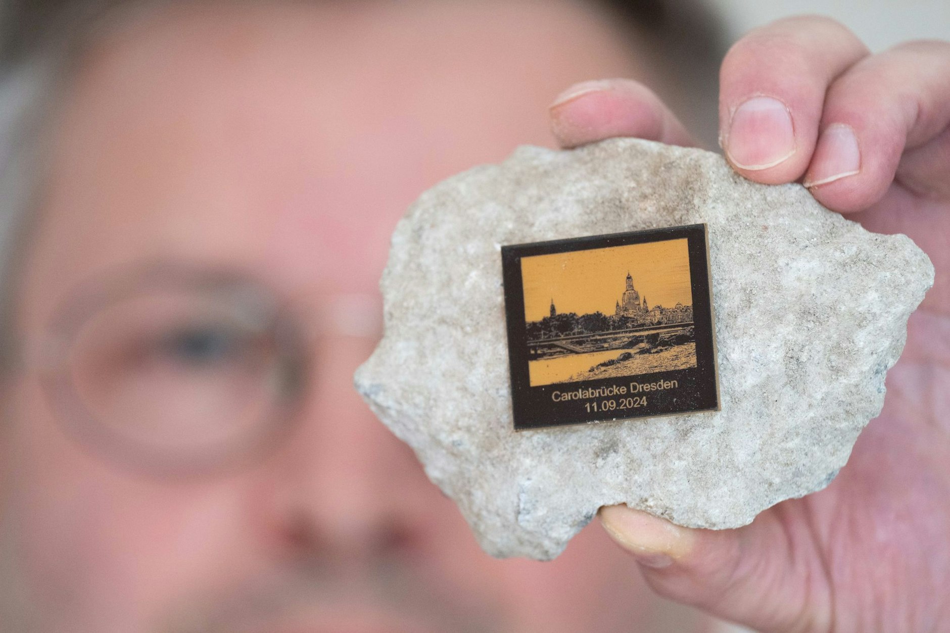 Torsten Daae mit einen Stein des abgerissenen Brückenteils C der eingestürzten Carolabrücke mit einer Plakette.