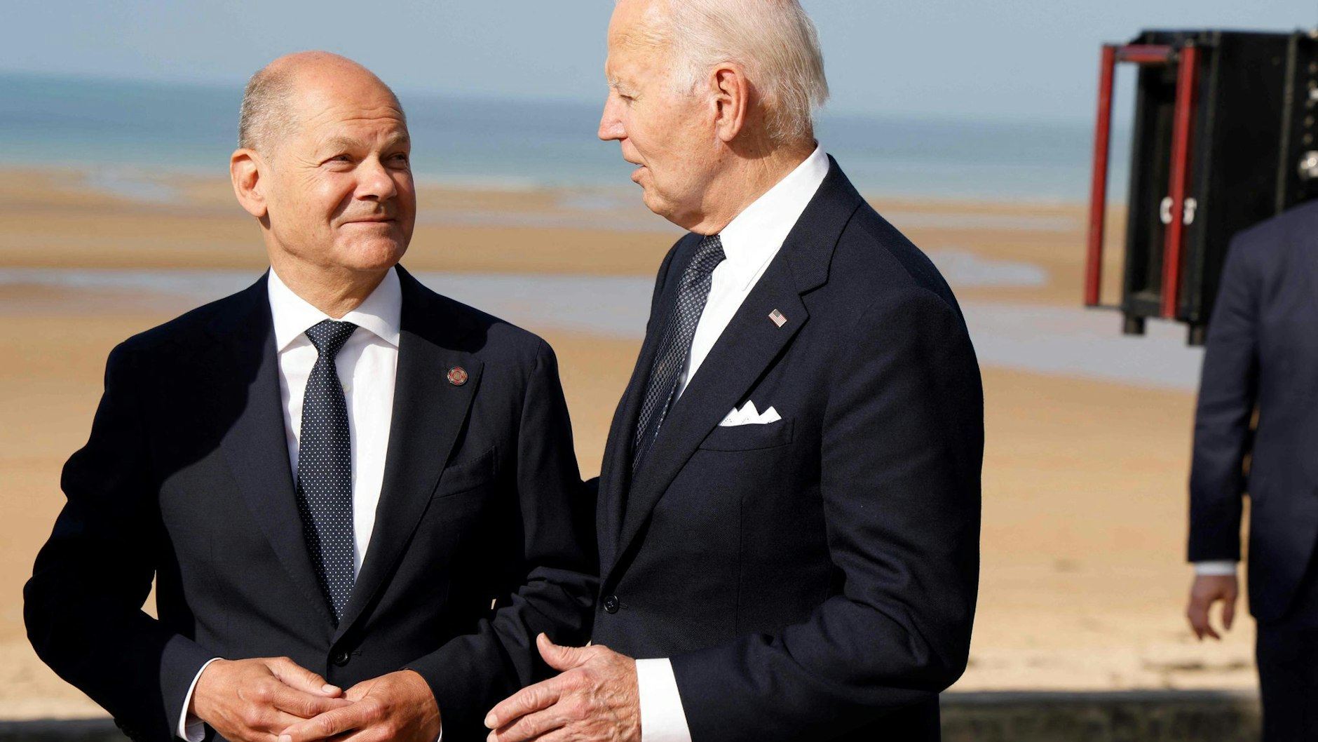 Bundeskanzler Olaf Scholz (l.) und US-Präsident Joe Biden unterhalten sich am Rande der internationalen Gedenkveranstaltung am 6. Juni 2024 zum 80. Jahrestag des D-Day am Omaha Beach.