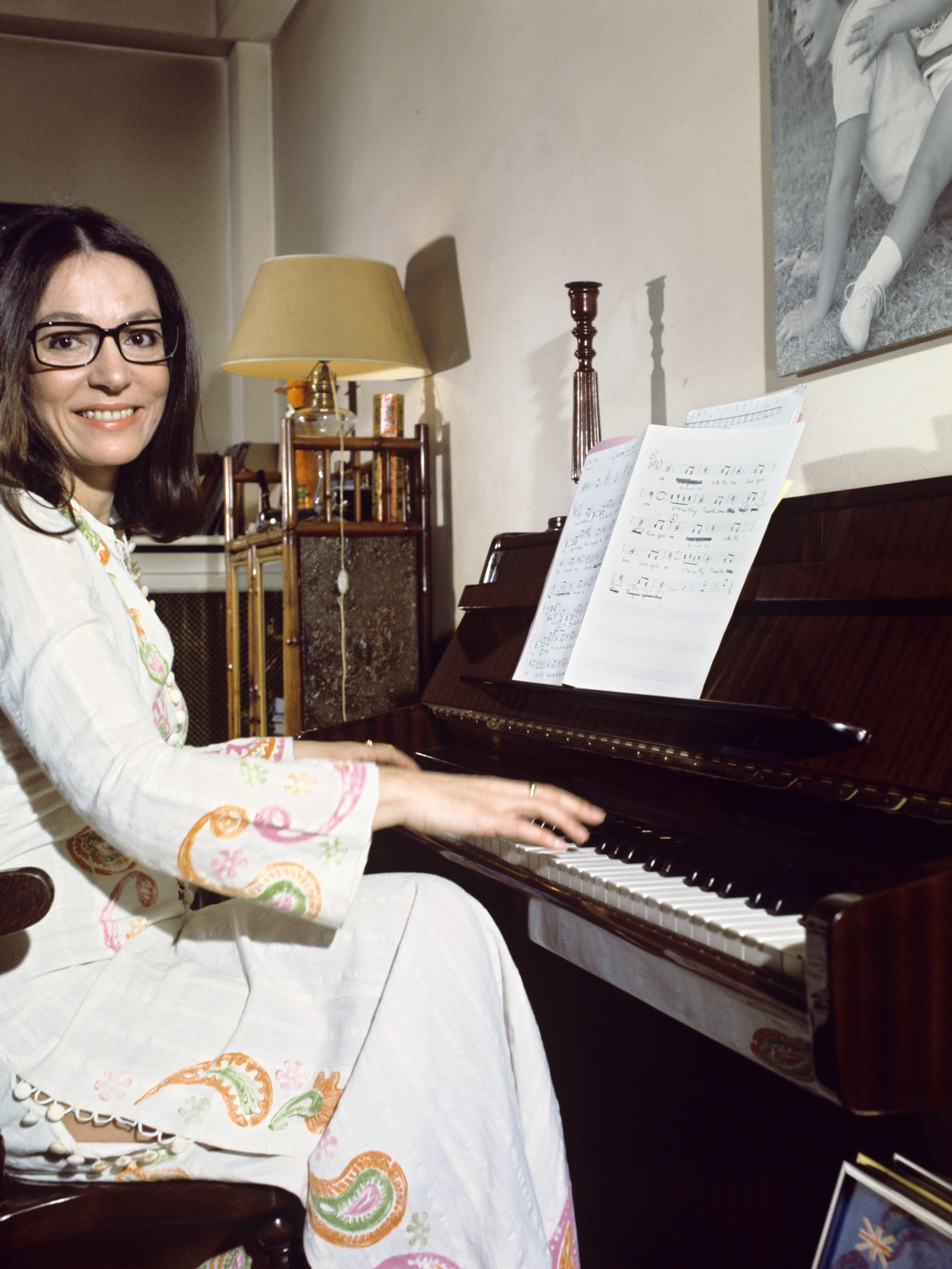 Die griechische Sängerin Nana Mouskouri sitzt an einem Klavier. Seit Jahrzehnten ist sie für viele Menschen die Stimme Griechenlands. Ihr Markenzeichen ist eine schwarze Brille.