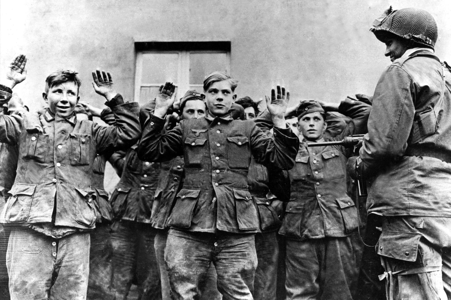 Junge deutsche Soldaten werden im Zweiten Weltkrieg nach ihrer Gefangennahme von einem US-amerikanischen Soldaten bewacht.