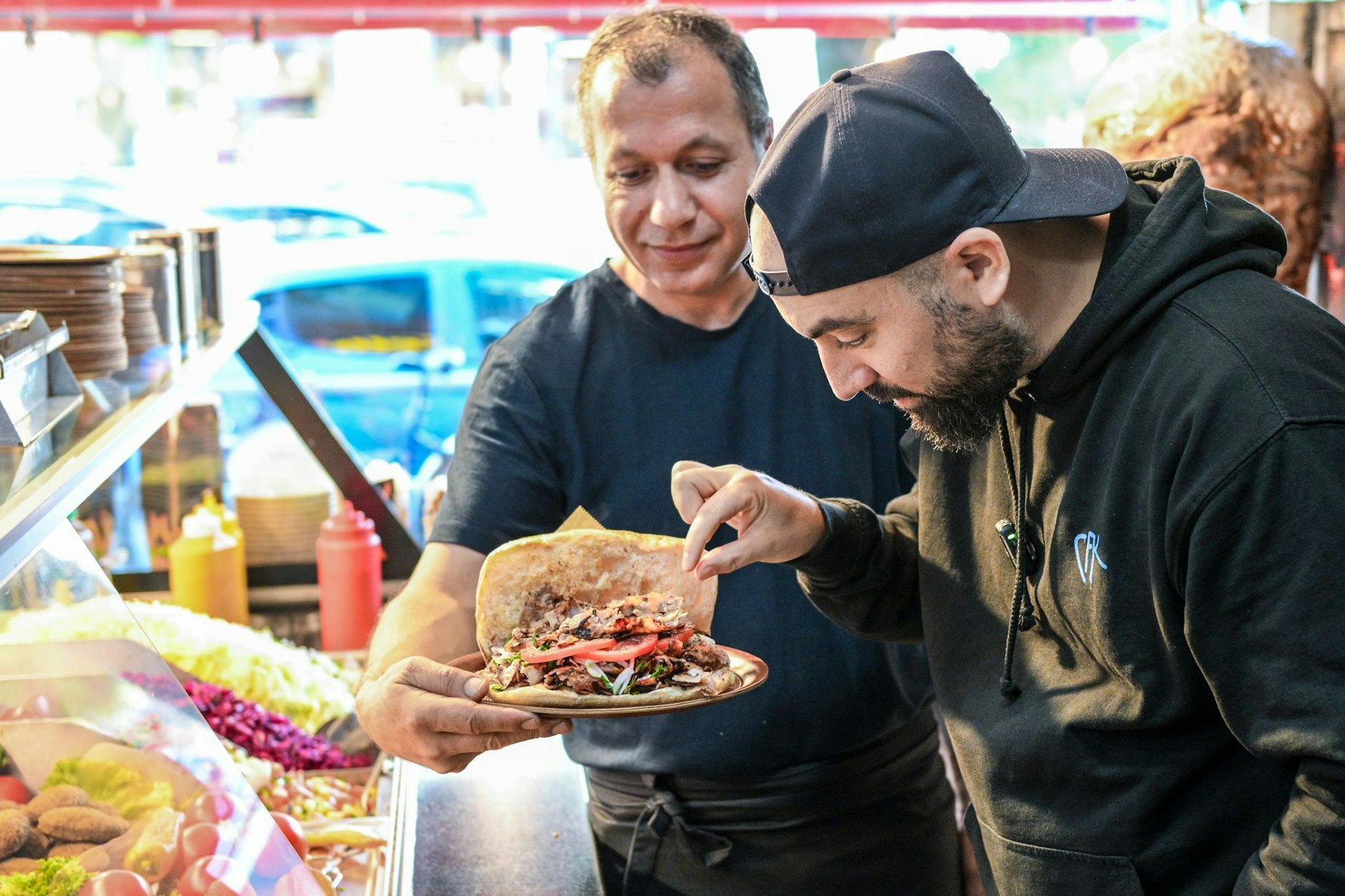 Influencer Can F. Kennedy (r) testet im Elbis-Döner von Inhaber Süleyman Sahin, der den vermeintlich besten Döner an der Line U9 anbietet.