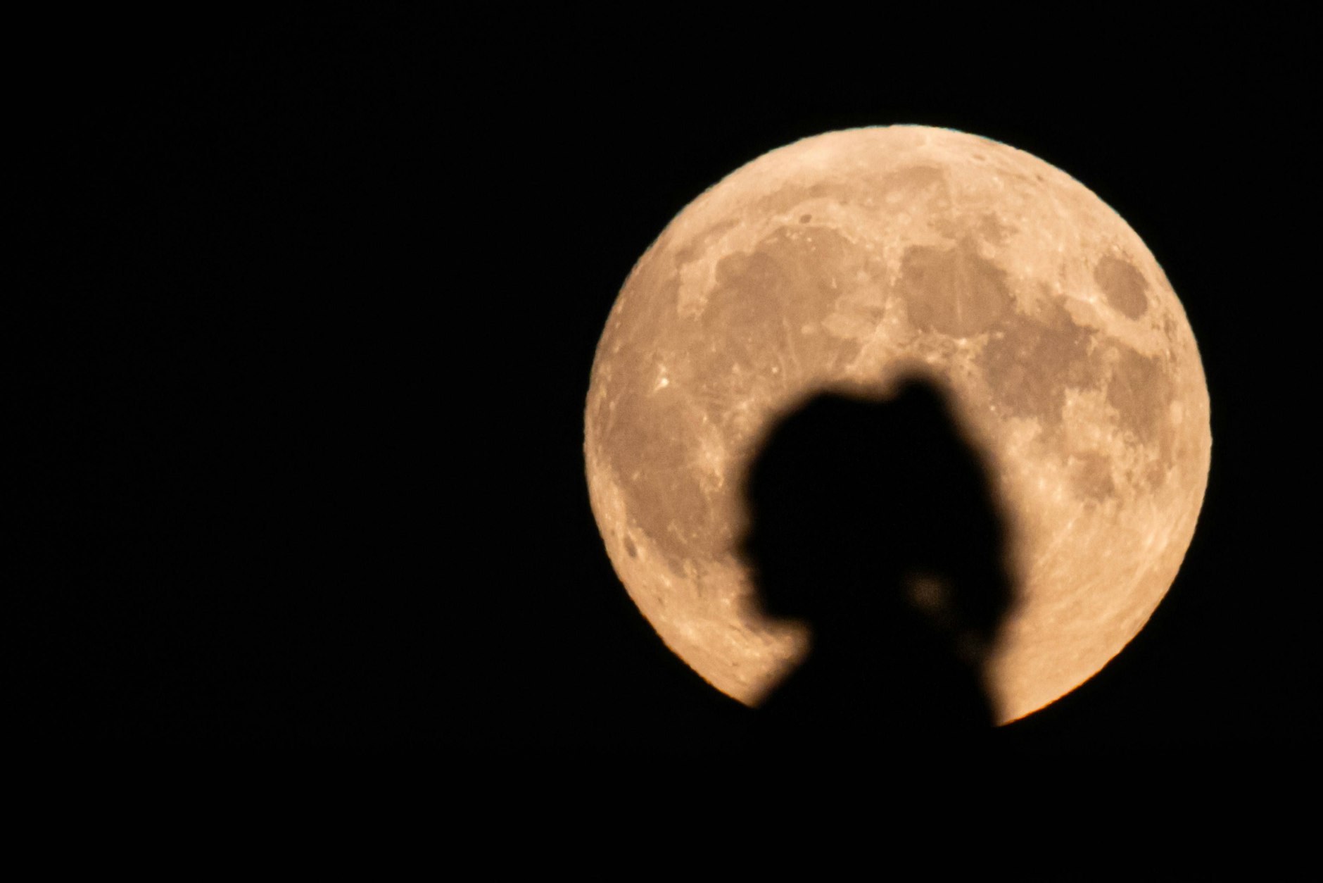 Die Silhouette einer Frau zeichnet sich vor dem aufgegangenen Vollmond ab.
