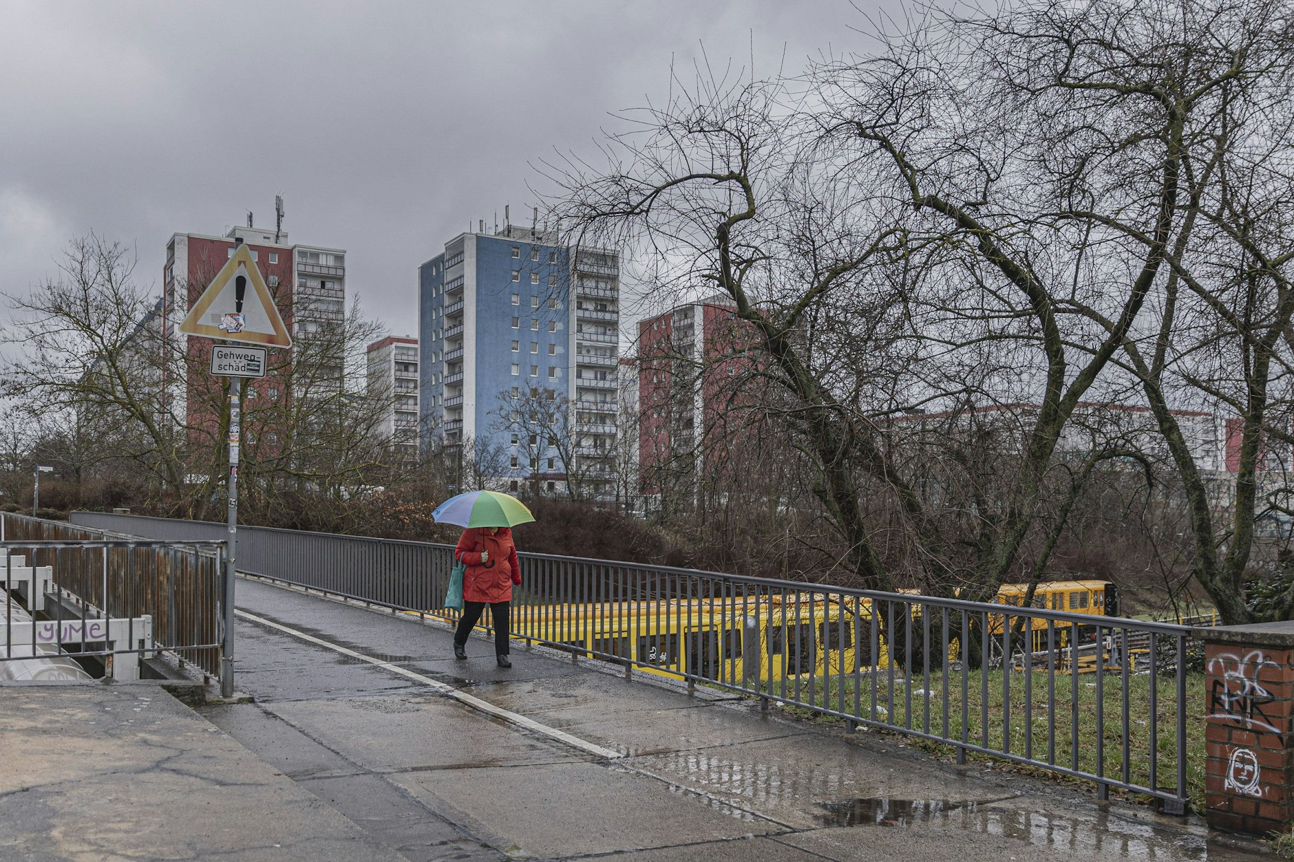 Eine Frau geht über eine Brücke, hinter ihr ein Wohnblock in Hellersdorf. Fremd in der eigenen Stadt zu sein, das fühlt sich für viele nicht gut an. 