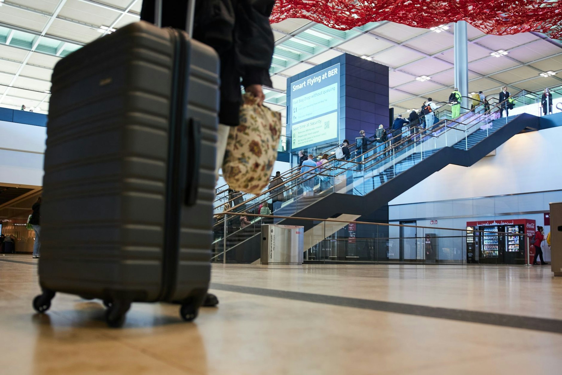 Menschen nehmen am Flughafen BER die Rolltreppe zu den Check-In-Schaltern. Der Besuch von US-Präsident Biden in Deutschland ist mit zahlreichen Verkehrseinschränkungen verbunden.