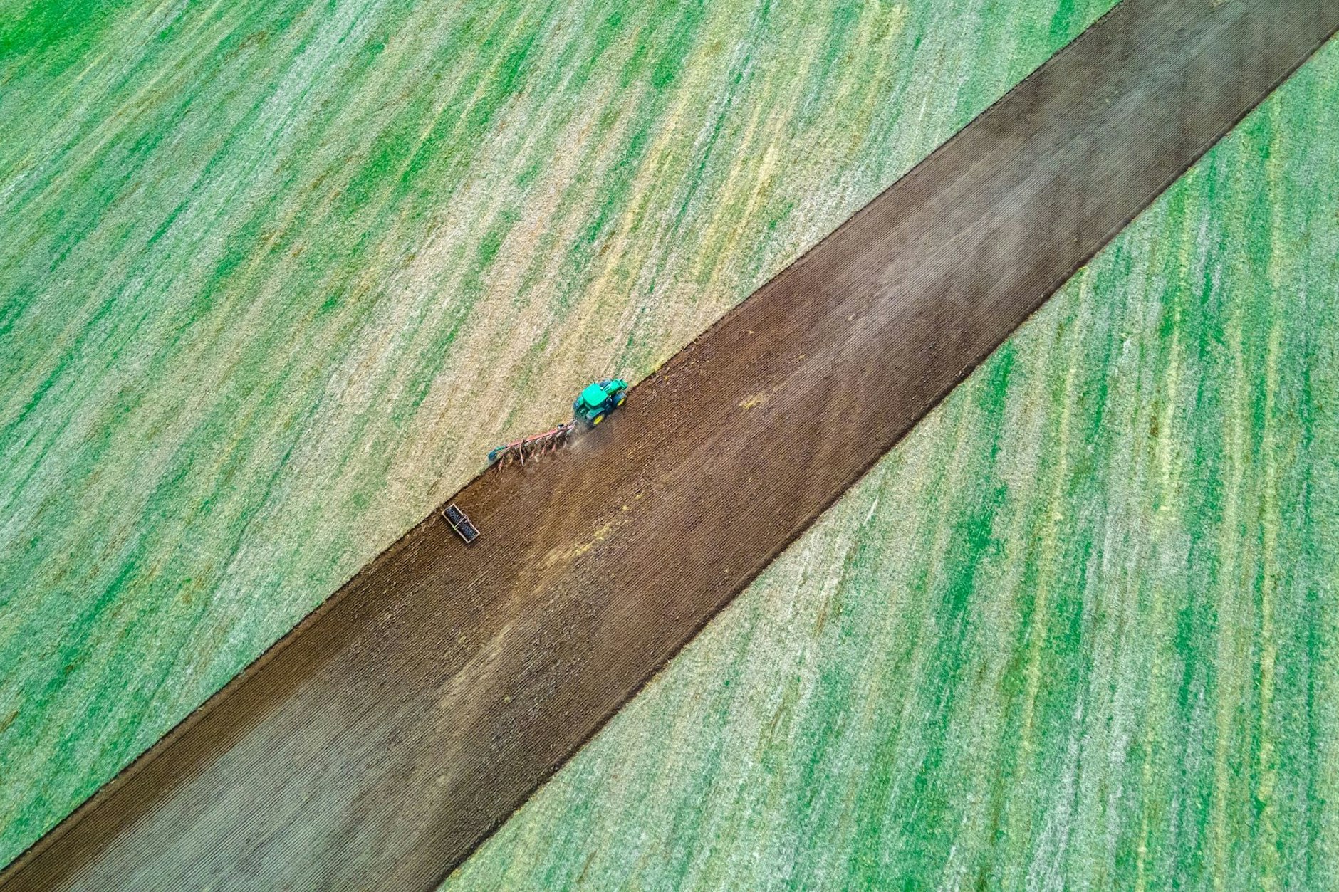 Ein Traktor zieht Pflug und Egge über ein abgeerntetes Feld.