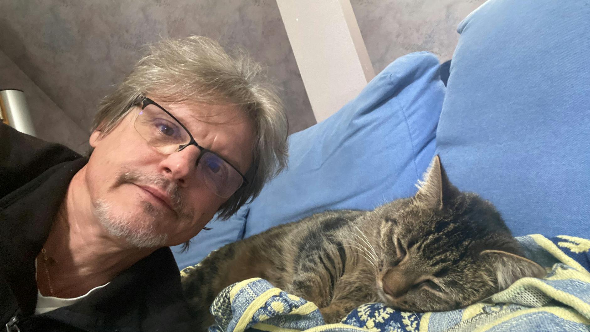 Norbert Koch-Klaucke mit der entlaufenden Katze, die zufrieden auf dem Sofa liegt. Der KURIER-Reporter weiß, das kleine Glück mit Twinkie ist nicht auf Dauer und sucht nach ihrem Besitzer.