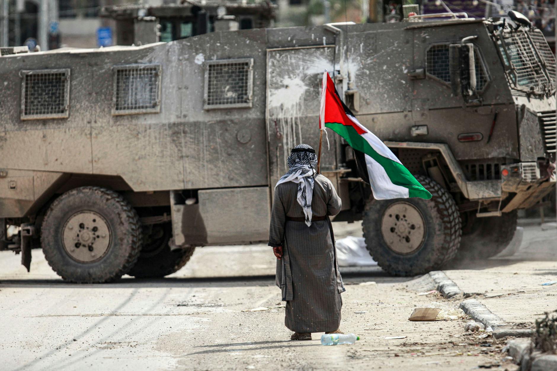 Gazastreifen: Ein älterer Mann steht mit einer palästinensischen Flagge in der Hand vor einem israelischen Militärfahrzeug.