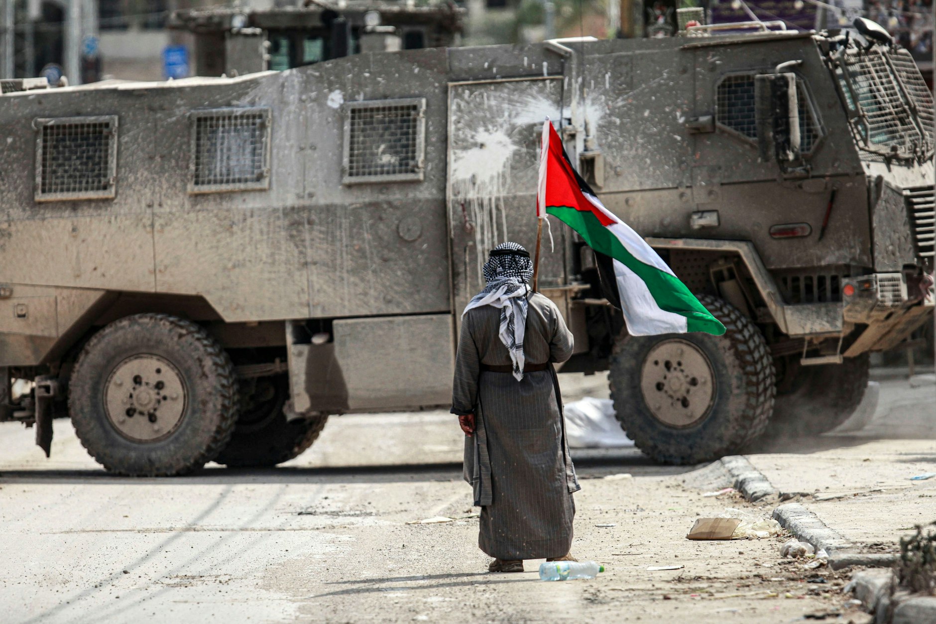 Gazastreifen: Ein älterer Mann steht mit einer palästinensischen Flagge in der Hand vor einem israelischen Militärfahrzeug.