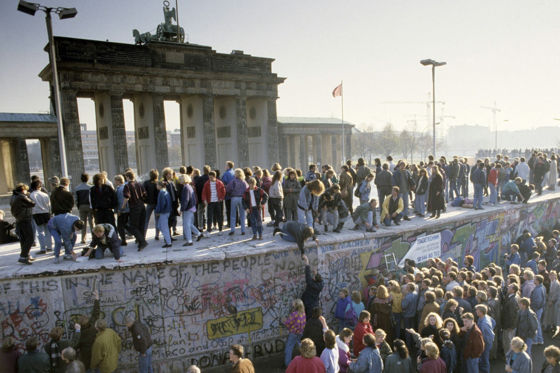 Menschenmassen auf und vor der Berliner Mauer am Brandenburger Tor während des Mauerfalls.