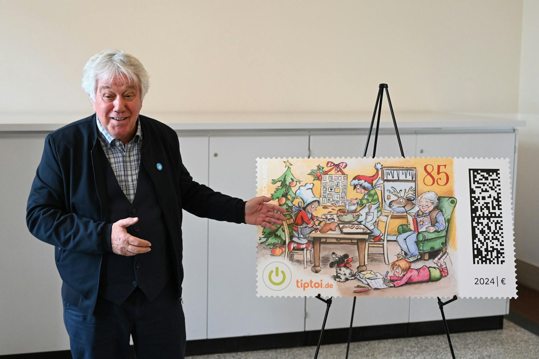 Der Liedermacher Rolf Zuckowski steht im Museum für Kommunikation neben der „ersten sprechenden und singenden Weihnachtsbriefmarke“ der Deutschen Post.