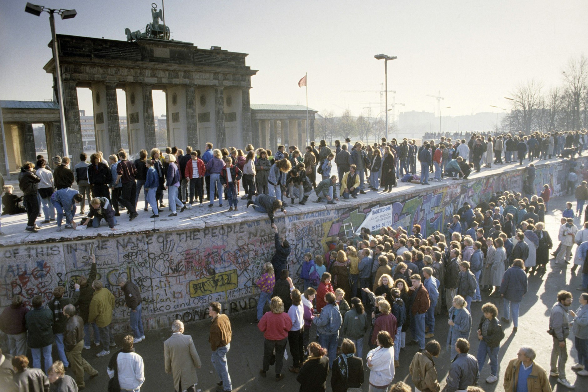 Menschenmassen auf und vor der Berliner Mauer am Brandenburger Tor während des Mauerfalls: ein ergreifender Tag, der heute noch unter die Haut geht. 