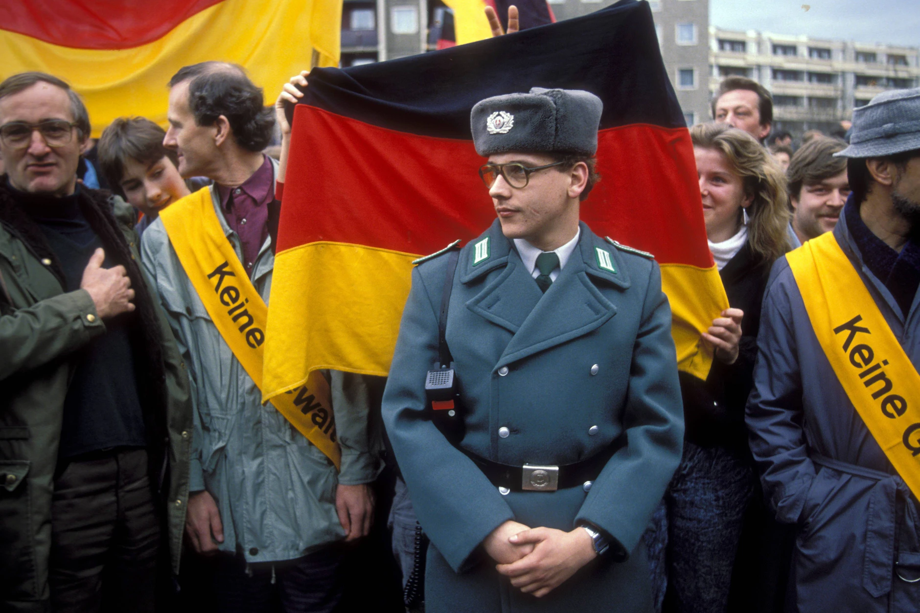 Volkspolizist vor BRD-Fahne whrend einer Demonstration zum Besuch von Helmut Kohl in Leipzig, Dezember 1989.