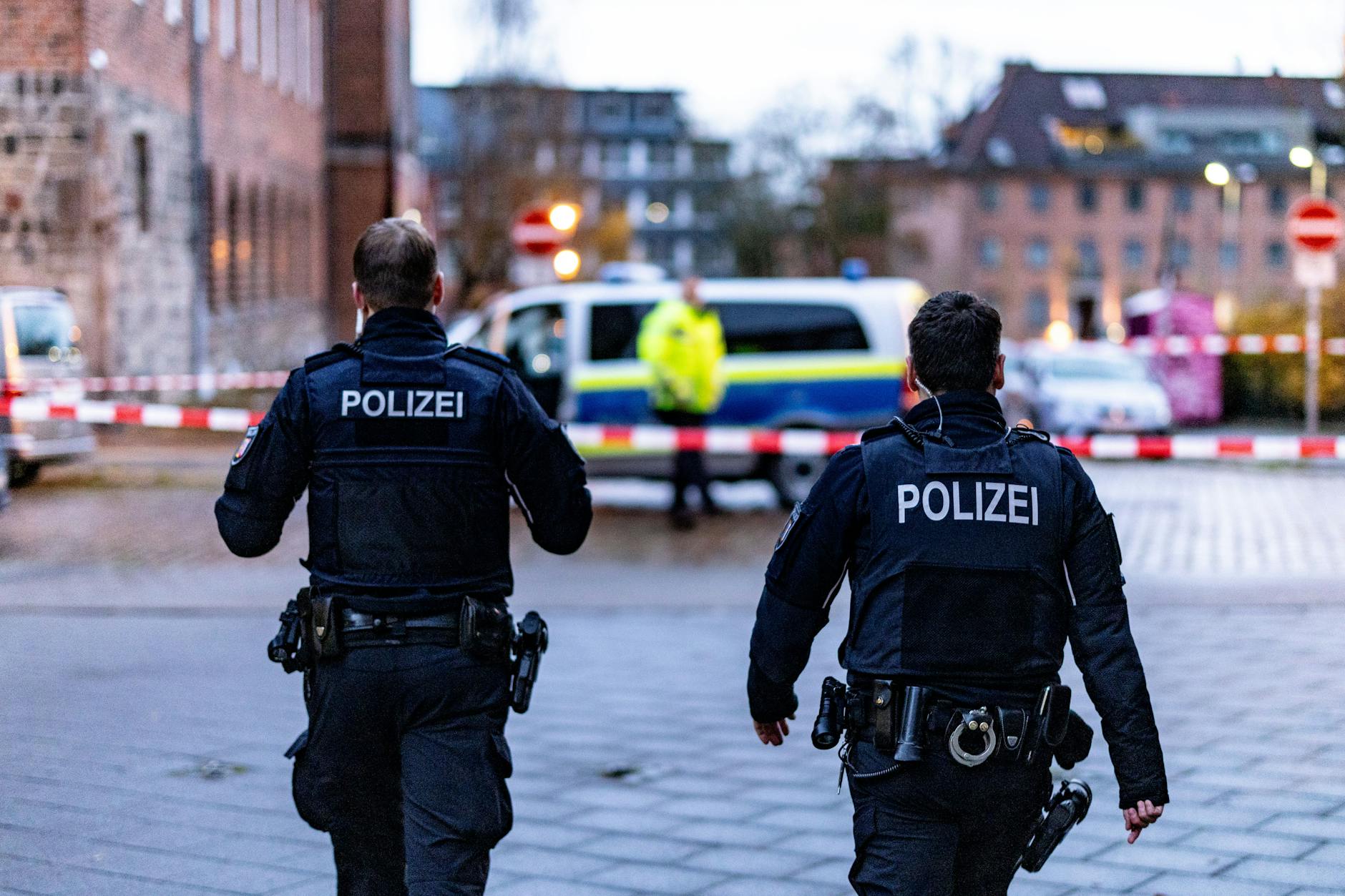 Zwei Polizeibeamte laufen auf die Absperrung vor einer Kieler Polizeidienststelle zu, an der Beamte auf einen Mann geschossen haben.