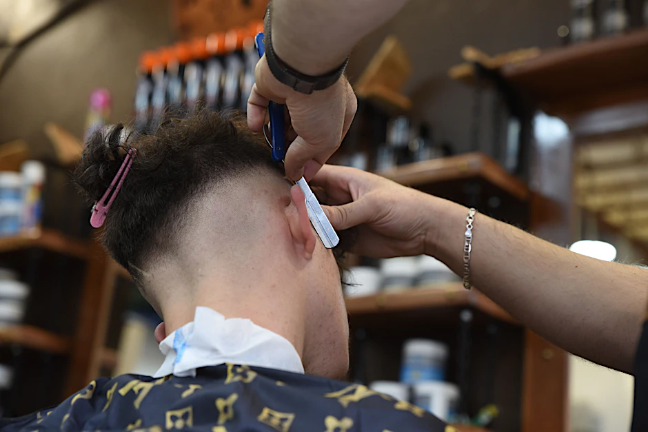 Ein Friseur rasiert in einem Barbershop die Haare eines Kunden.