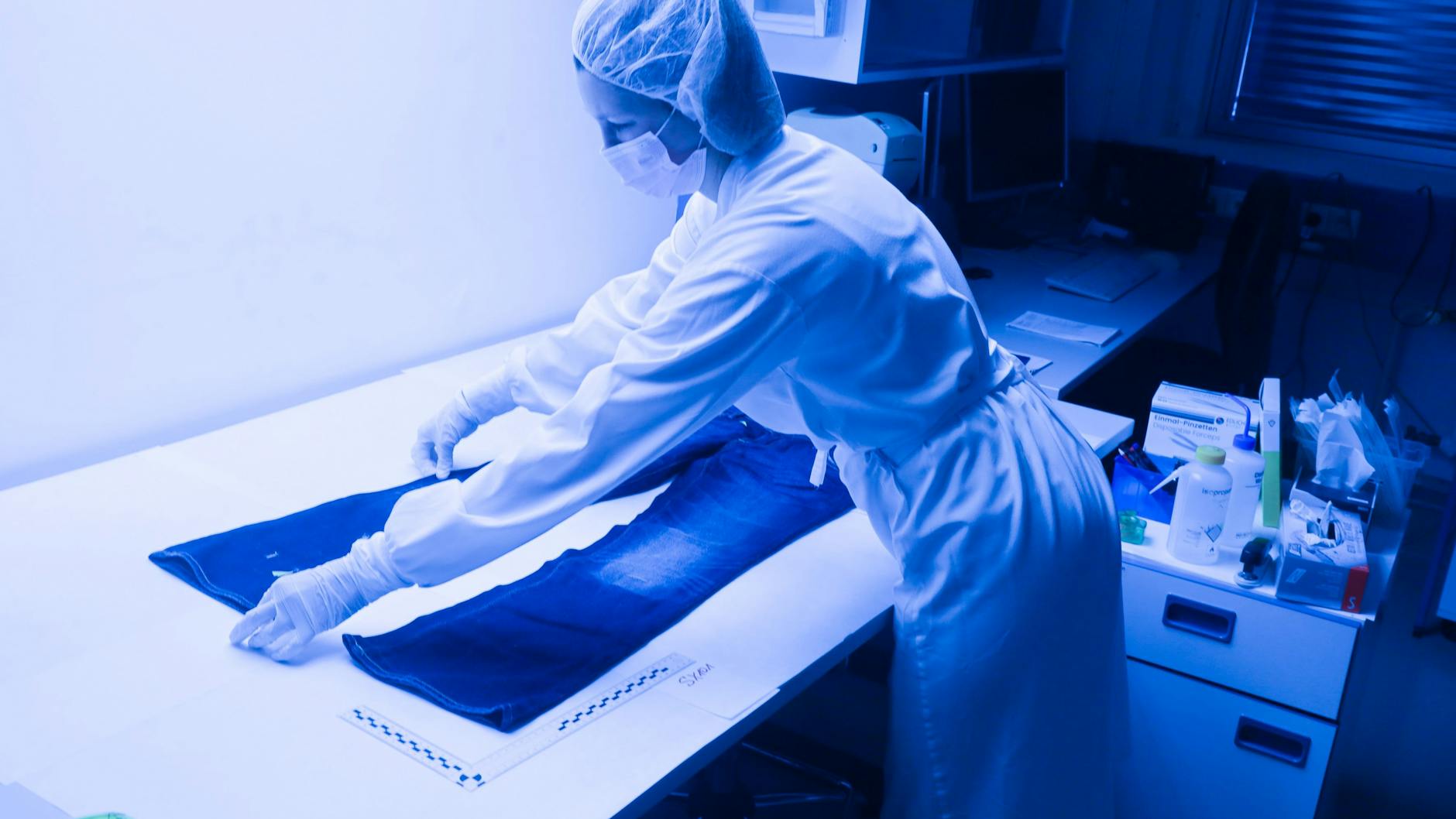 Eine kriminaltechnische Assistentin untersucht eine Jeans nach Spuren.