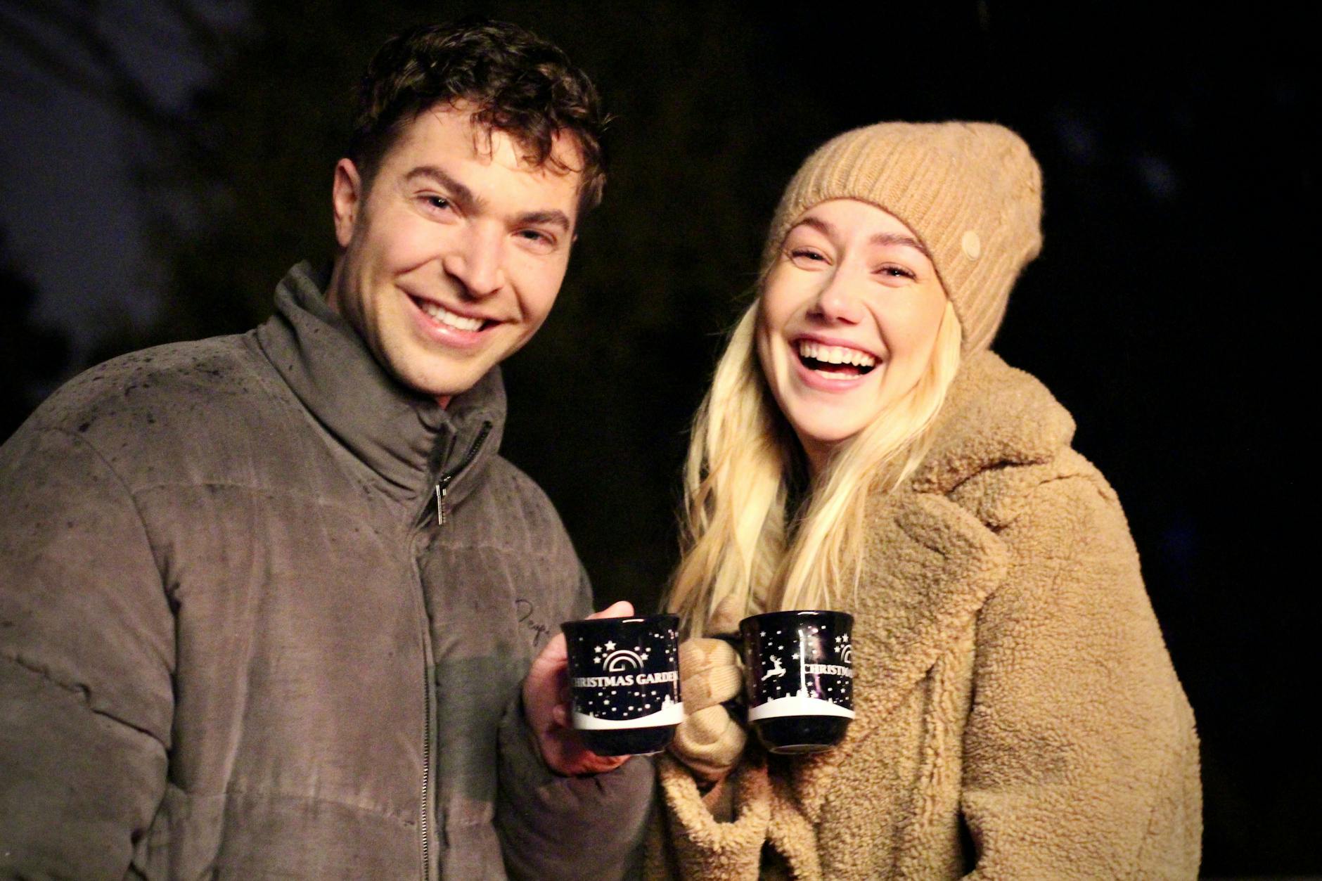 Schlagerstar Julian David und die Unternehmerin Annalena Kaiser, Teil der fröhlichen Gruppe, genießen gemeinsam die zauberhafte Stimmung im „Christmas Garden Berlin“. „Stößchen“ mit Punsch und Glühwein!