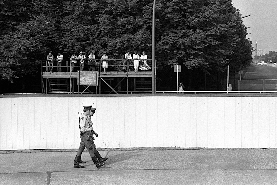 Westberliner Touristen beobachten Soldaten der Grenztruppen der DDR während ihrer Patrouille an der Berliner Mauer.