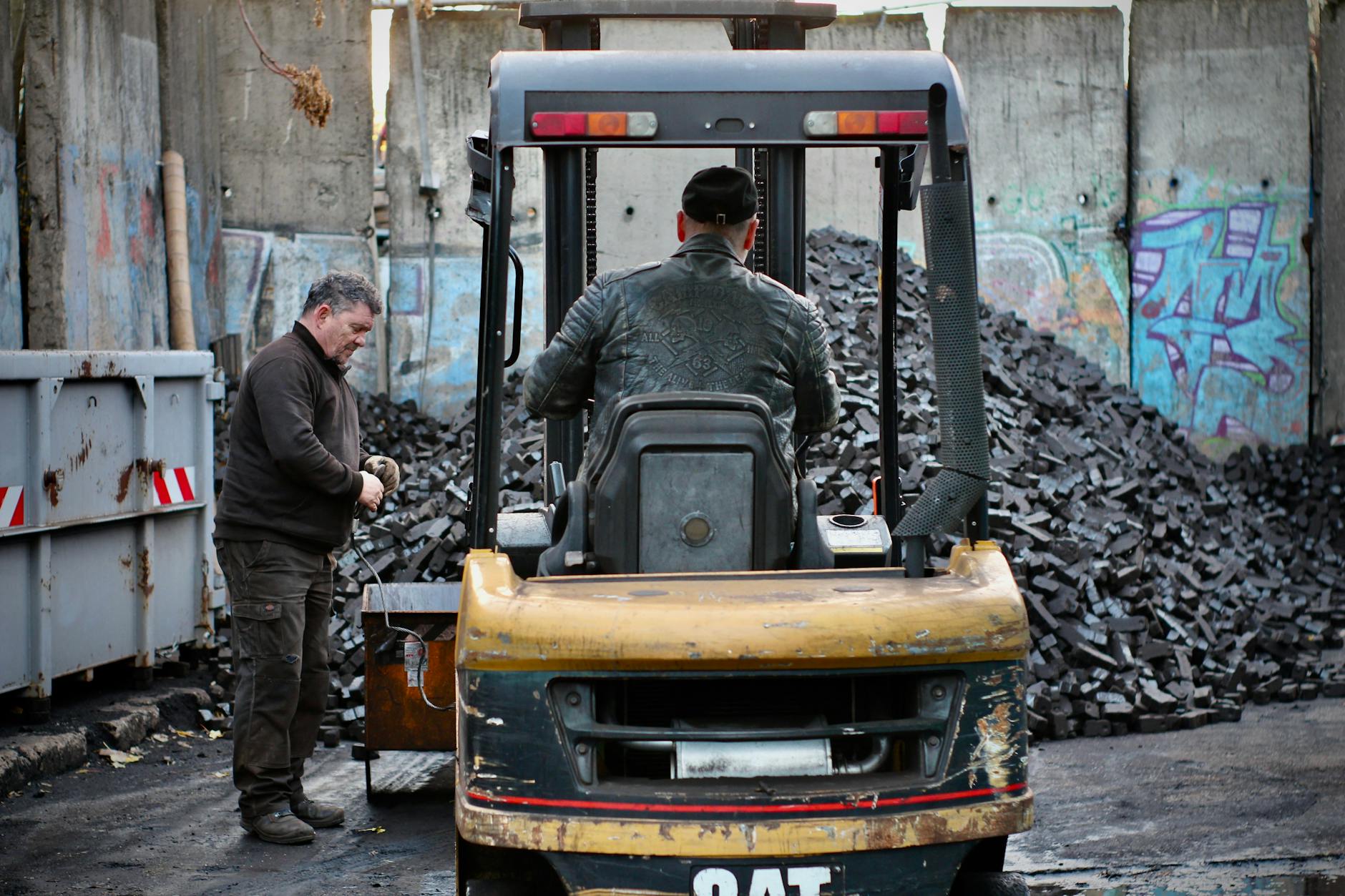 Im Prenzlauer Berg lagert die Kohle der Firma Braun – auf einem Grundstück, das von Teilen der Berliner Mauer umzäunt ist. Nach dem Mauerfall wurden Grenzstreifen an die Industrie vergeben, doch das Gelände schrumpfte über die Jahre erheblich. Hier sieht man Firmenbesitzer Arnd auf dem Gabelstapler, beim Verladen der Kohle vor der Ausfahrt.