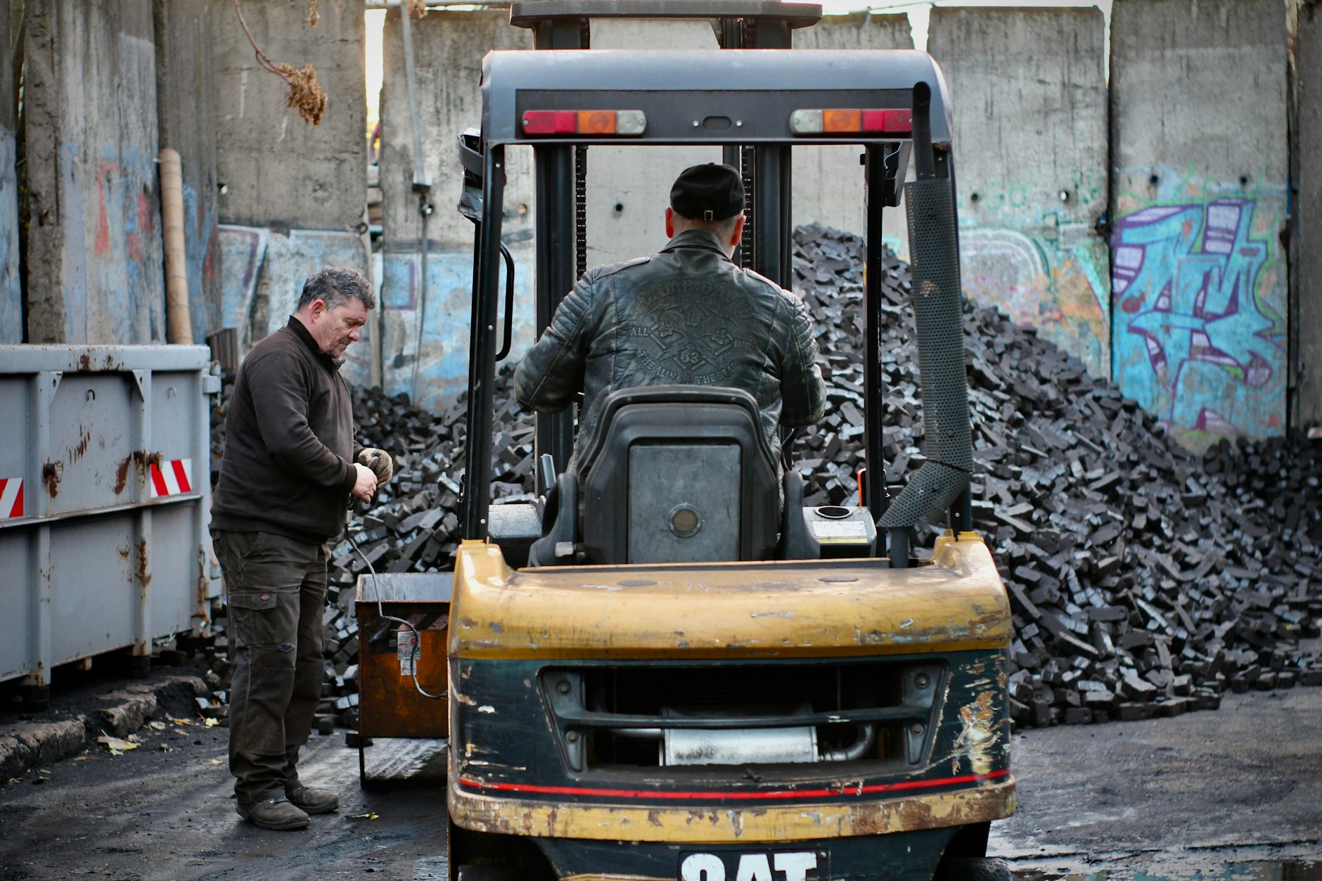 Im Prenzlauer Berg lagert die Kohle der Firma Braun – auf einem Grundstück, das von Teilen der Berliner Mauer umzäunt ist. Nach dem Mauerfall wurden Grenzstreifen an die Industrie vergeben, doch das Gelände schrumpfte über die Jahre erheblich. Hier sieht man Firmenbesitzer Arnd auf dem Gabelstapler, beim Verladen der Kohle vor der Ausfahrt.