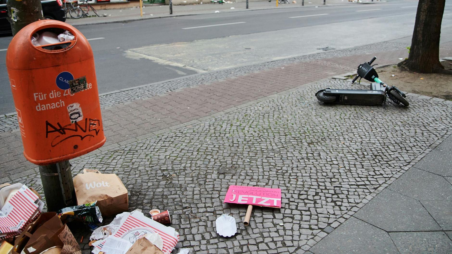 Ein Plakat und Müll liegen in Neukölln unter einem Mülleimer.