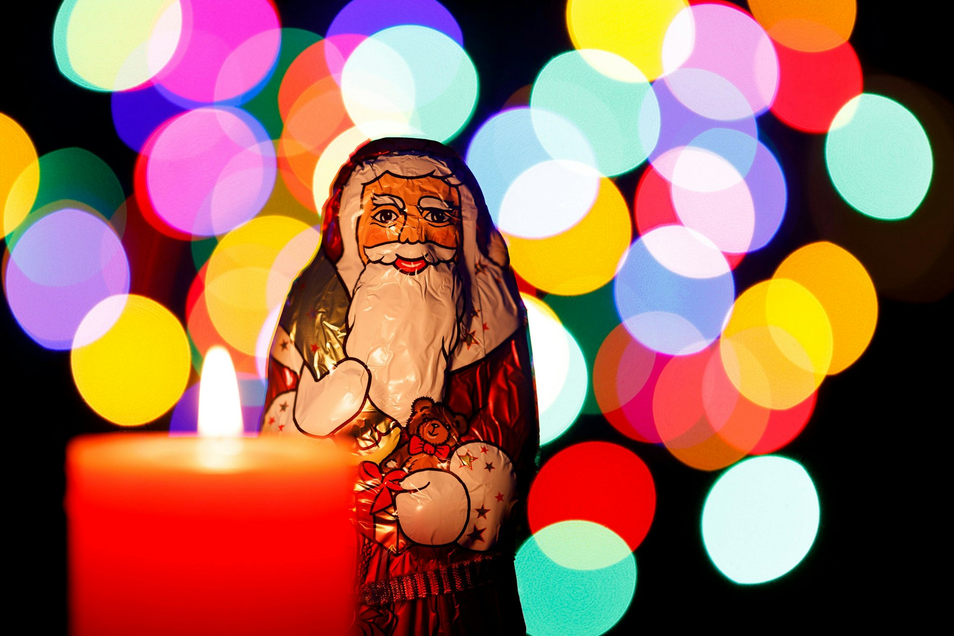 Ein Schoko-Weihnachtsmann von Lindt steht vor einer brennenden Adventskerze.