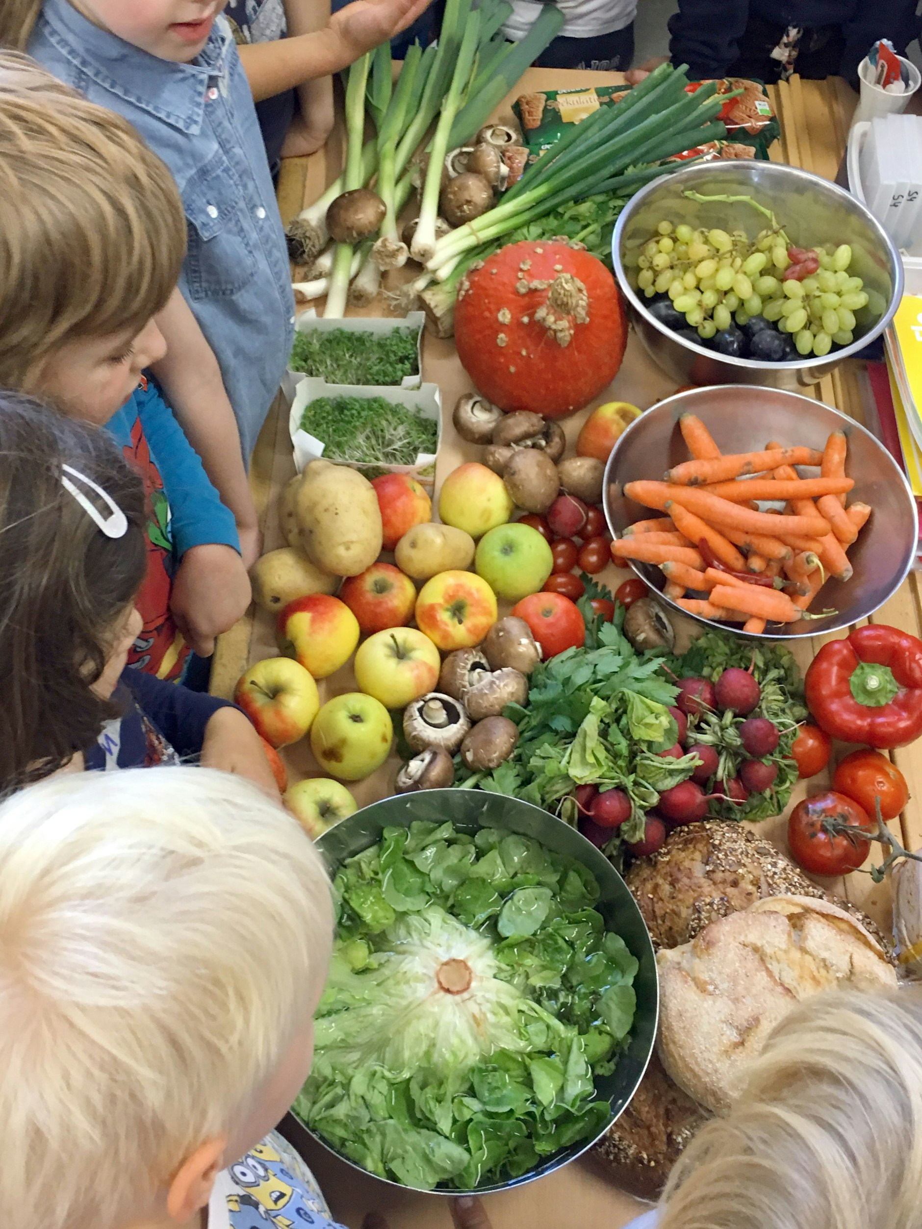 Berliner Grundschüler stehen während eines Bildungsworkshops von Restlos Glücklich an einem Tisch, auf dem Obst, Gemüse und Brot liegt.