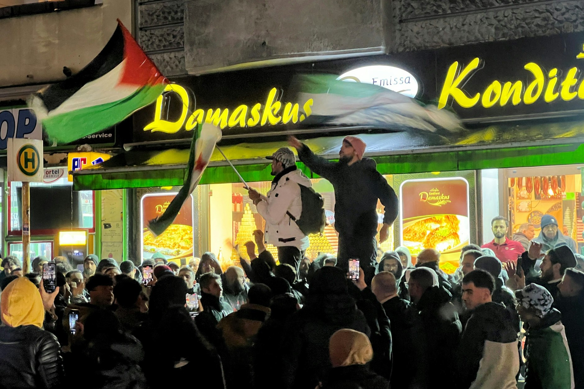 Berlin: Syrer versammeln sich im Bezirk Neukölln mit Flaggen vor der Bäckerei Damaskus und feiern den Vormarsch der Rebellen auf Damaskus.
