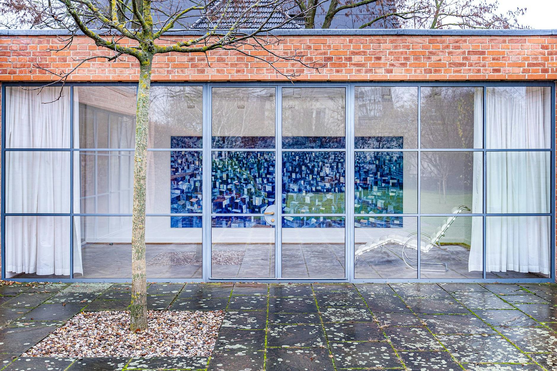 Die Südost-Fensterfront des Mies-Bungalows am Obersee. In der Galerie des einstigen Wohnhauses Lemke füllt David Schnells geometrisches Häuserpanorama „Kongress“ (Öl auf Leinwand, 2024) die ganze Wand.