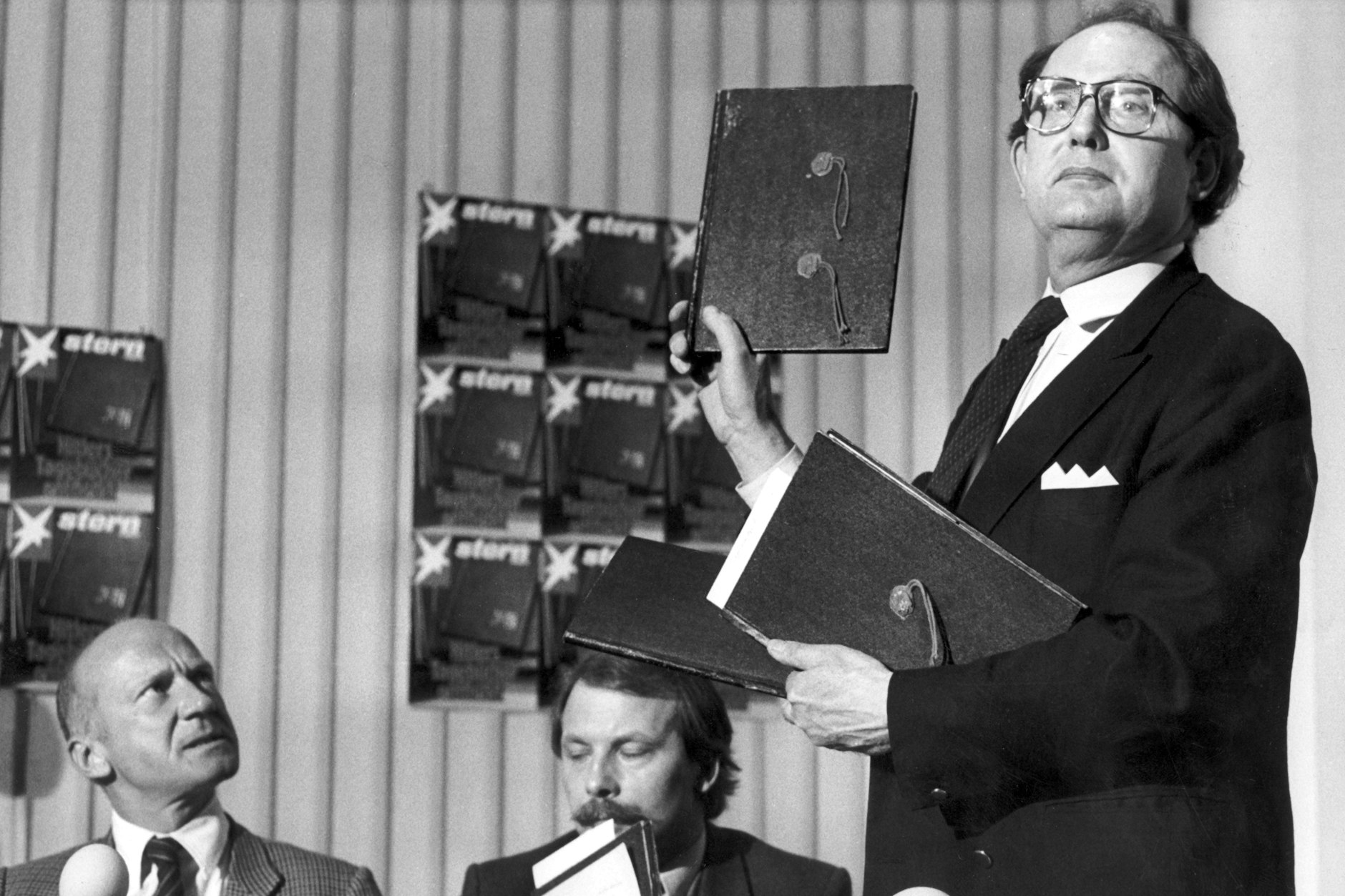 Stern-Reporter Gerd Heidemann (r.) zeigt am 25. April 1983 in Hamburg auf einer Pressekonferenz die vermeintlichen Hitler-Tagebücher. Links Chefredakteur Peter Koch, in der Mitte Redakteur Thomas Walde.