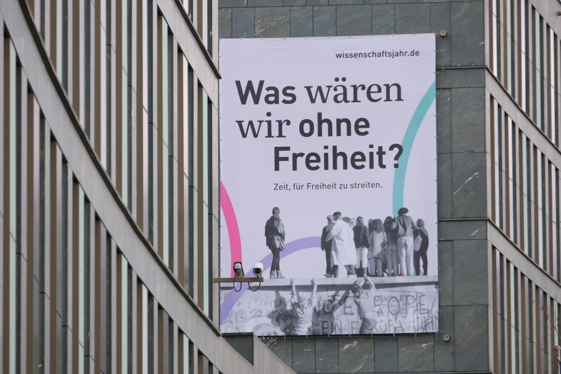 Das Plakat am Bundesbildungsministerium wirbt für die Freiheit – und nimmt sich die Freiheit zur Geschichtsklitterung: West-Berliner besteigen die Mauer am Brandenburger Tor, um in den Osten zu gaffen.