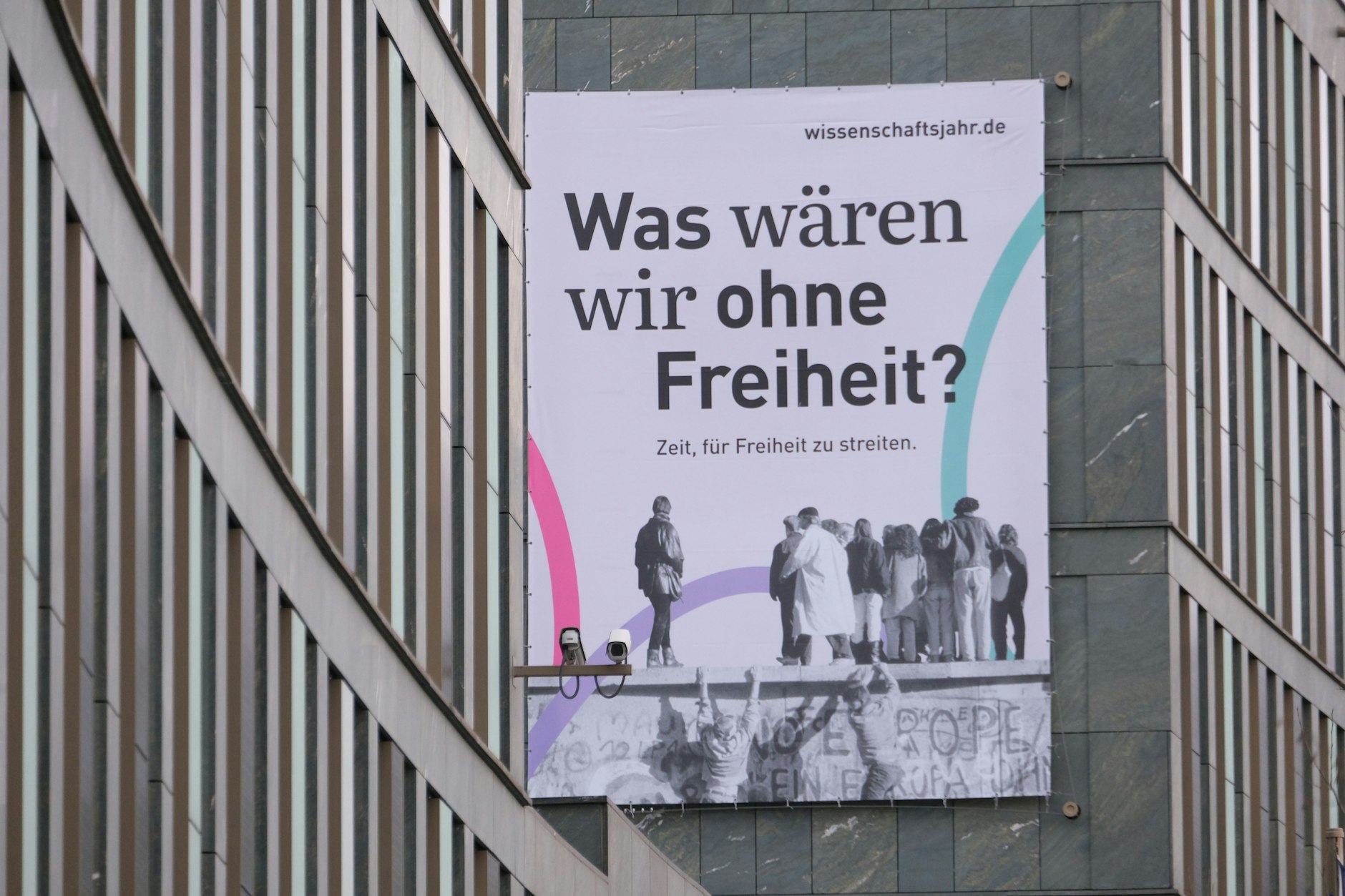 Das Plakat am Bundesbildungsministerium wirbt für die Freiheit – und nimmt sich die Freiheit zur Geschichtsklitterung: West-Berliner besteigen die Mauer am Brandenburger Tor, um in den Osten zu gaffen.