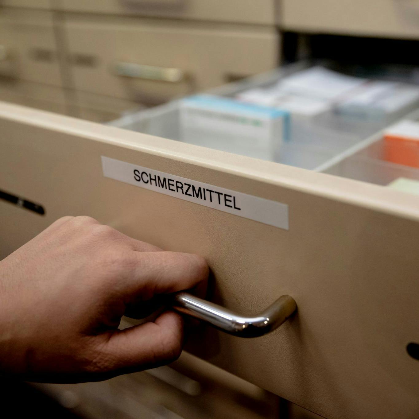 Eine Apothekerin öffnet in einer Apotheke eine mit „Schmerzmittel" beschriftete Schublade.