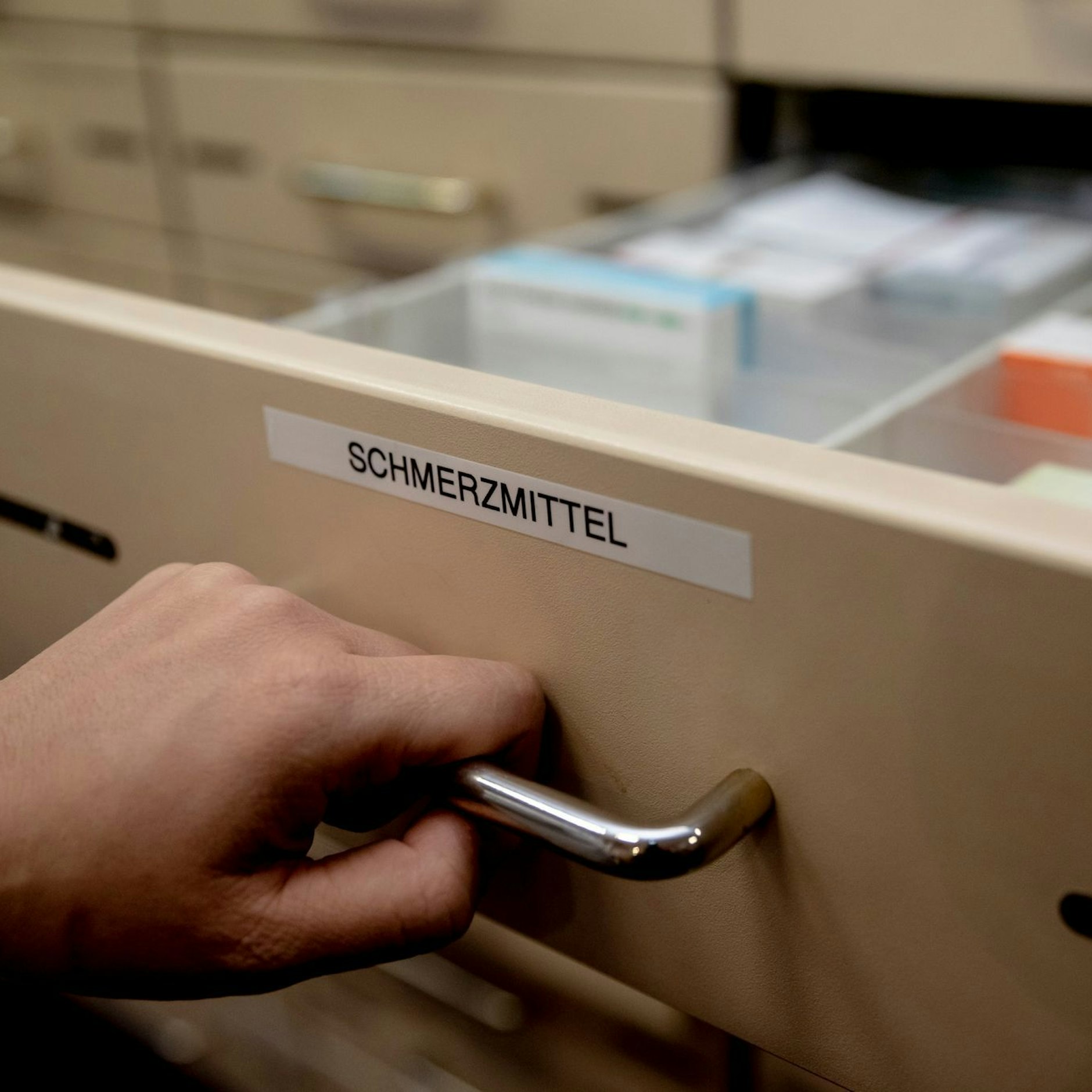 Eine Apothekerin öffnet in einer Apotheke eine mit „Schmerzmittel" beschriftete Schublade.