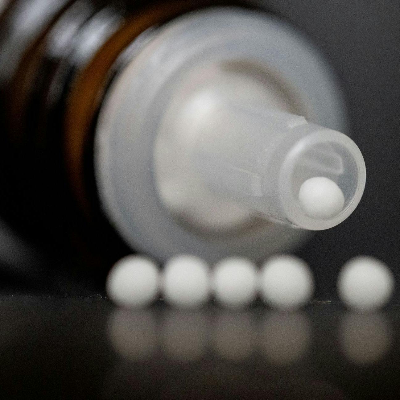 Homöopathische Kugeln liegen vor einer Spenderflasche auf einem Tisch.