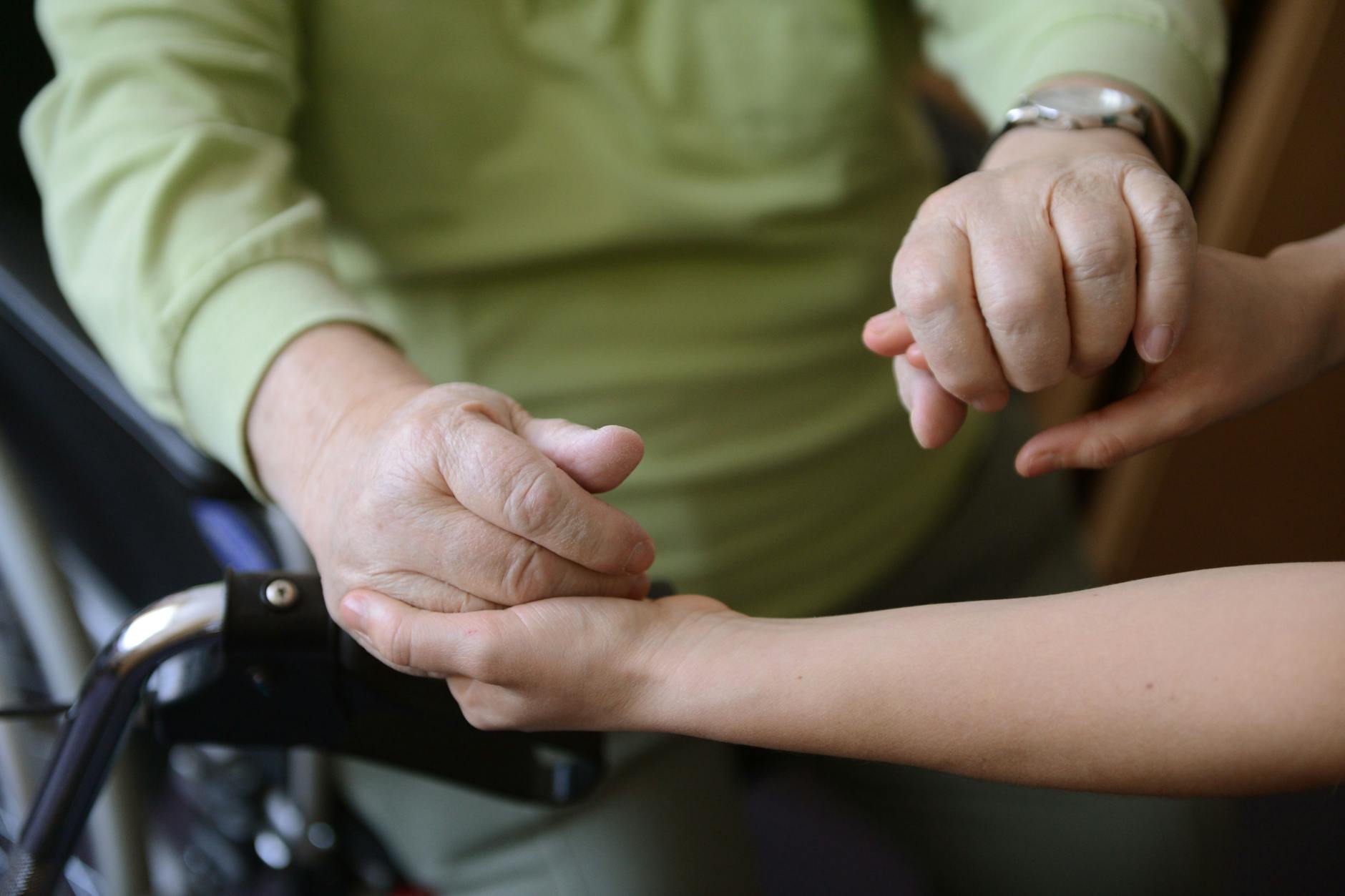 Eine junge Frau hält die Hände eines alten Mannes.